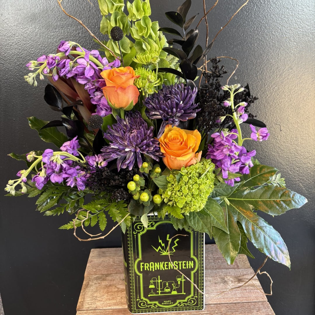 Orange roses and purple flowers arranged in a Frankenstein tin container
