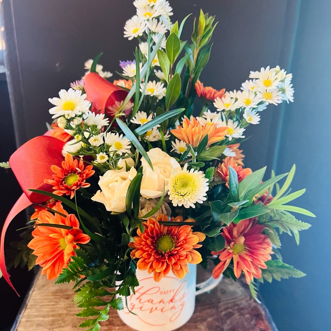 Mixed bouquet in a white mug with orange and white flowers and red ribbon