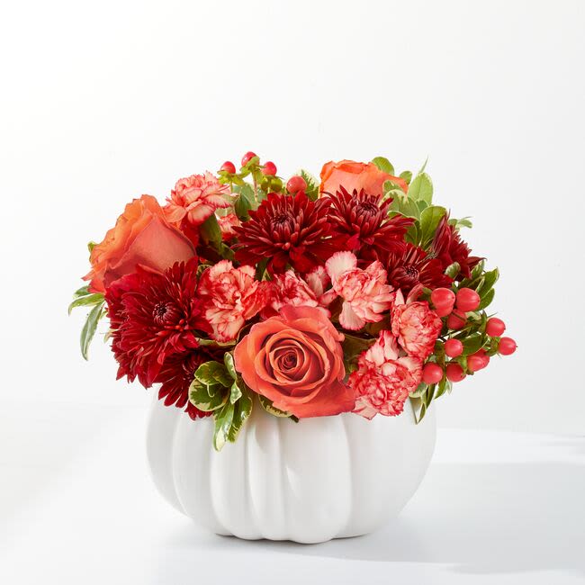Orange roses and red flowers arranged in a white pumpkin vase