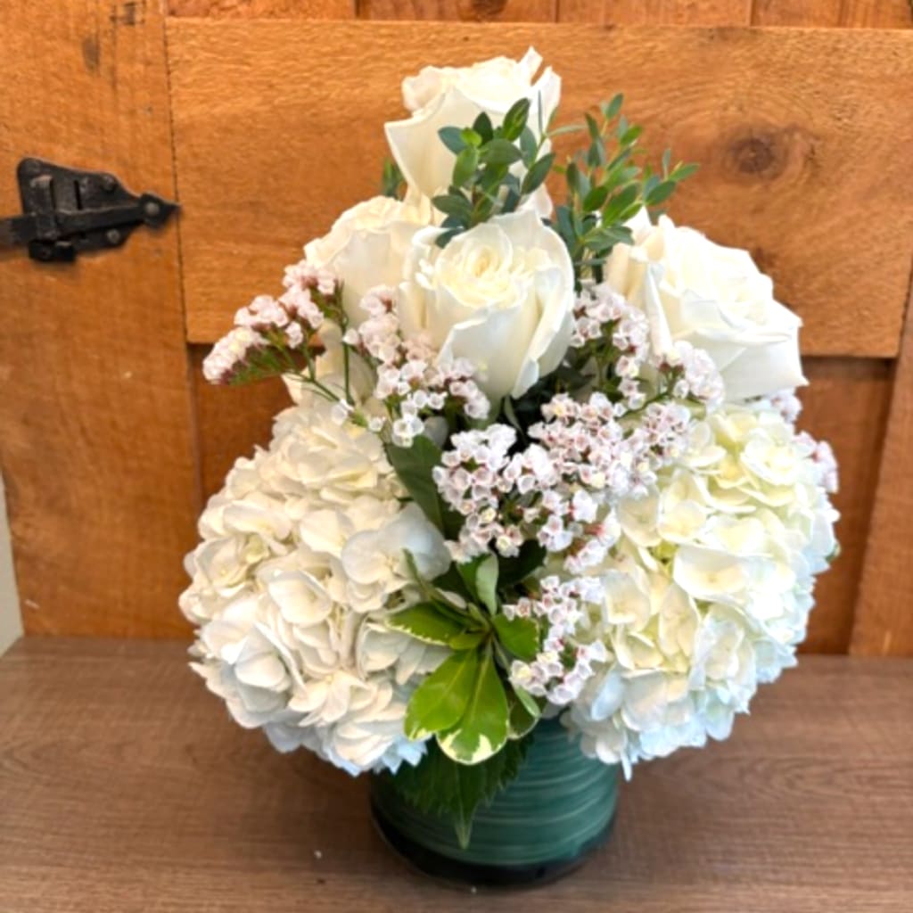White roses and hydrangeas in a green vase with small pink filler flowers