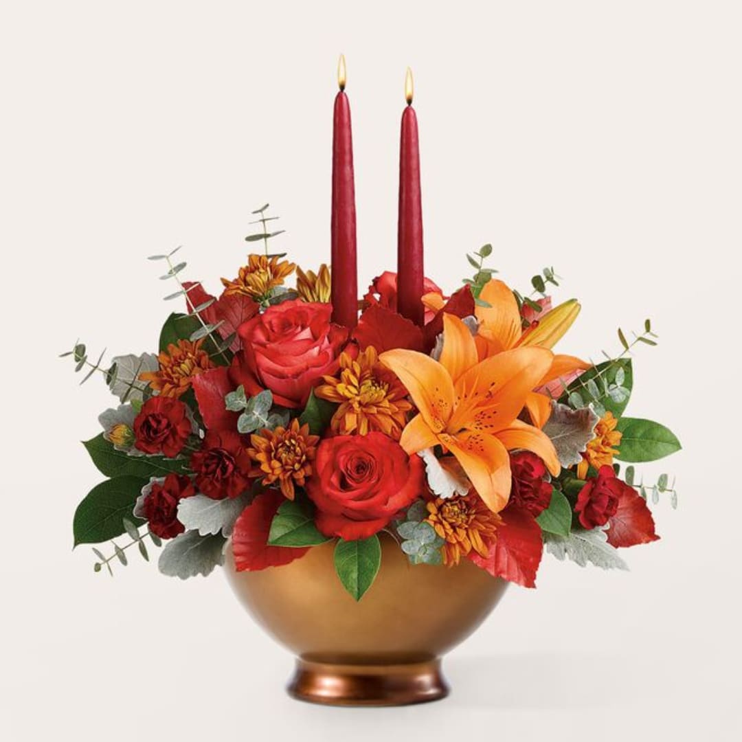 Red and orange floral arrangement with two tall red candles in a gold bowl