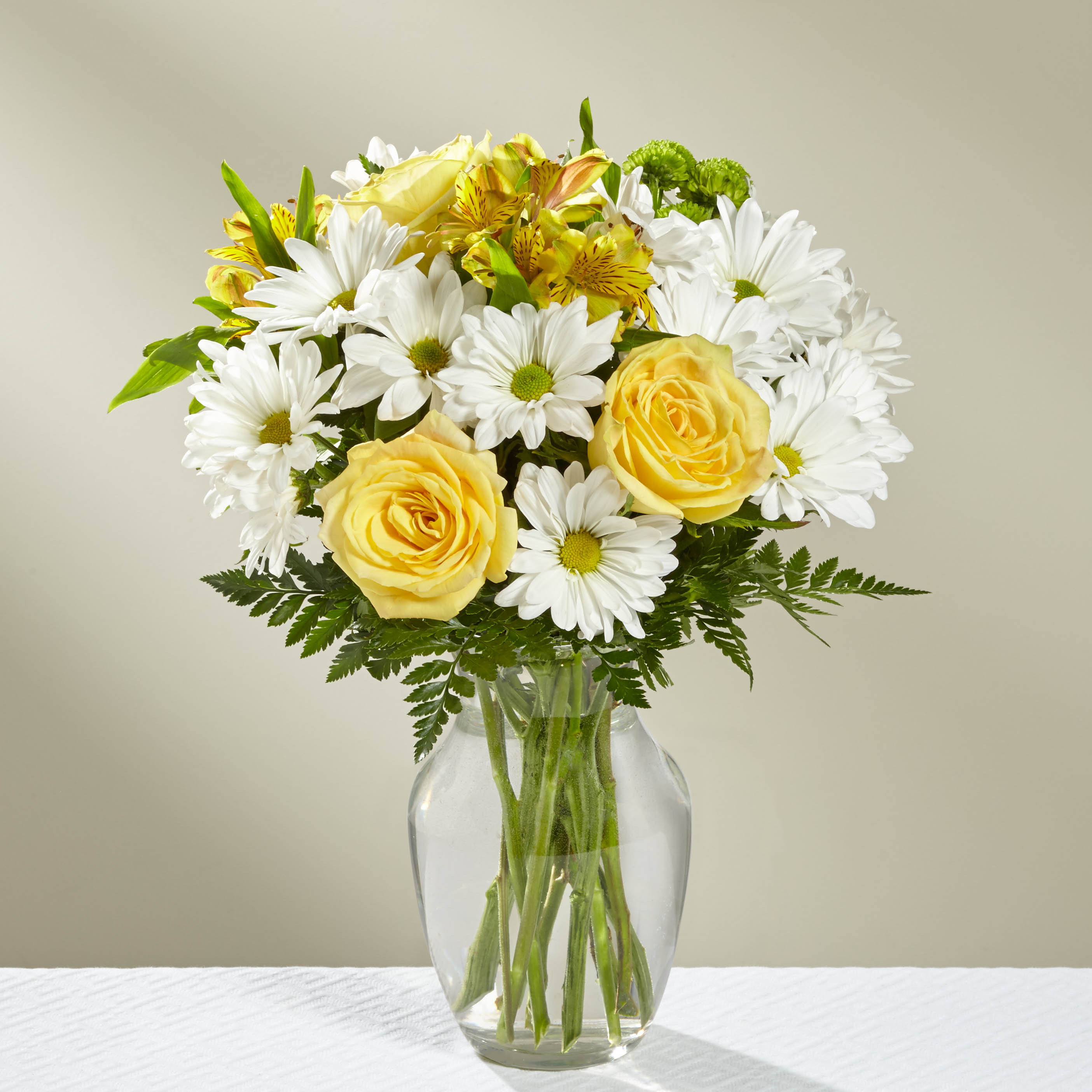 Yellow roses and white daisies in a clear glass vase