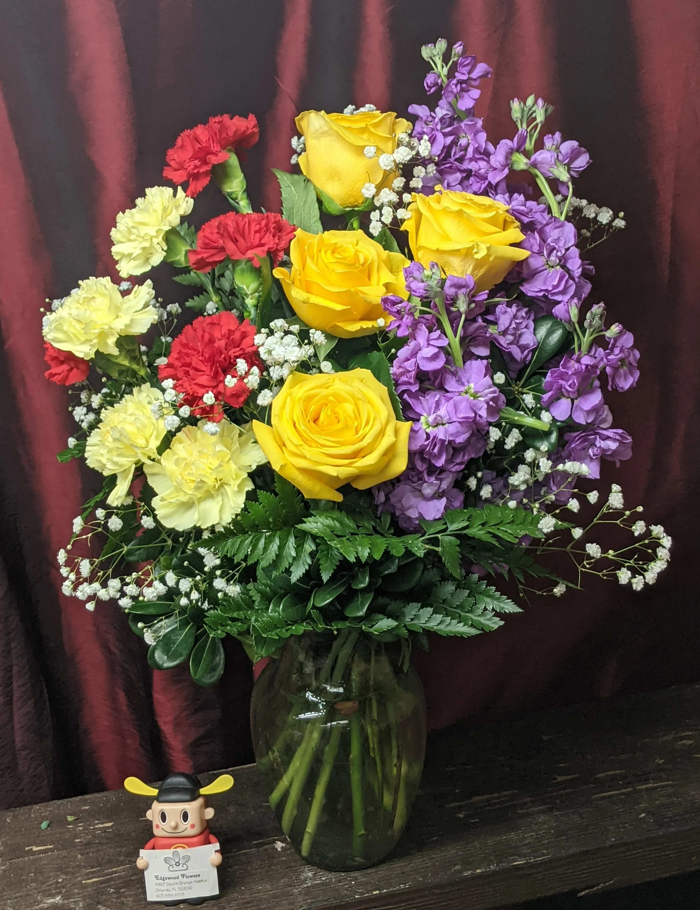 Bouquet of yellow roses, purple stock, and red and pale yellow carnations in a glass vase