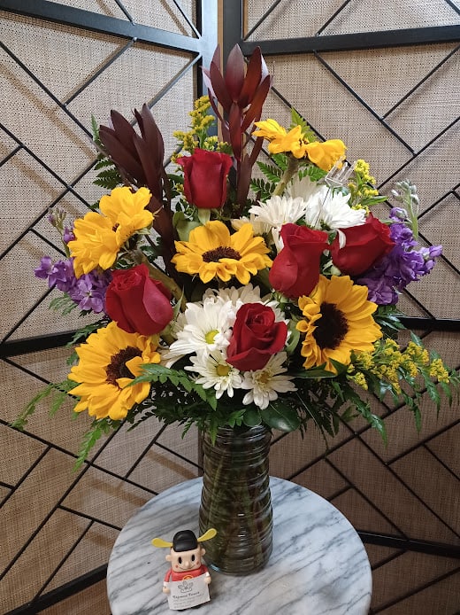 Mixed bouquet of red roses, sunflowers, and white daisies in a glass vase
