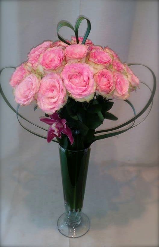 Pink roses arranged in a tall glass vase with wire heart loops