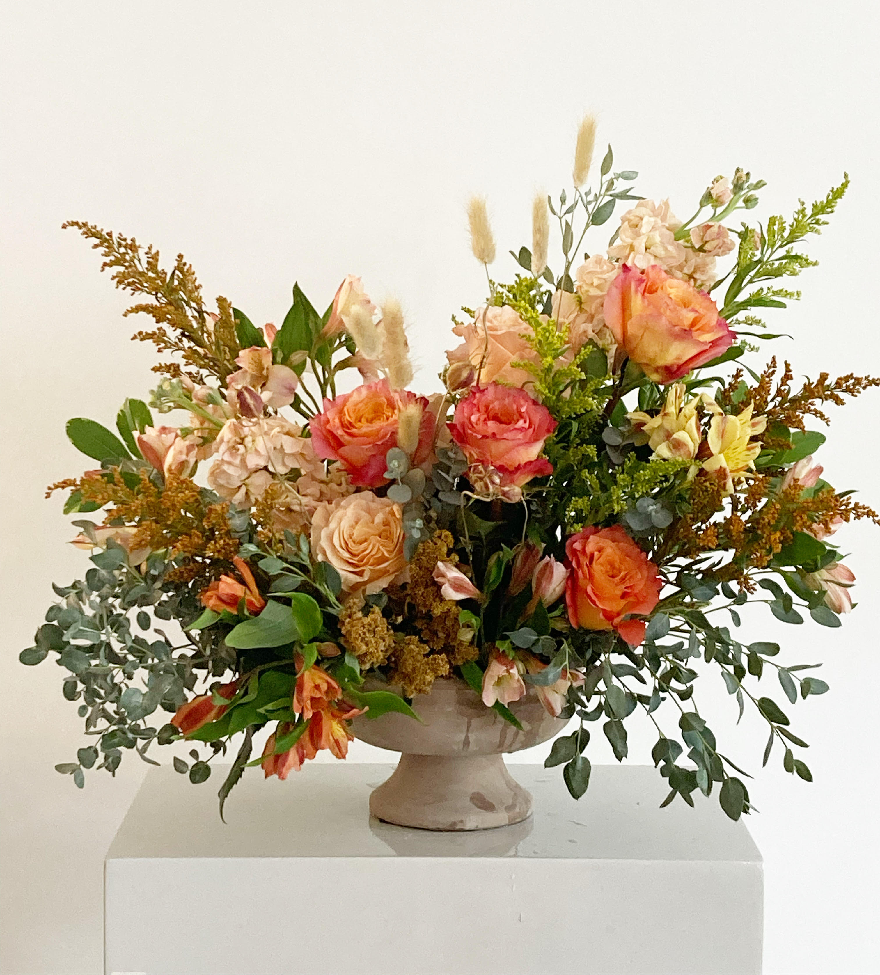 Peach and coral rose arrangement in a pedestal vase