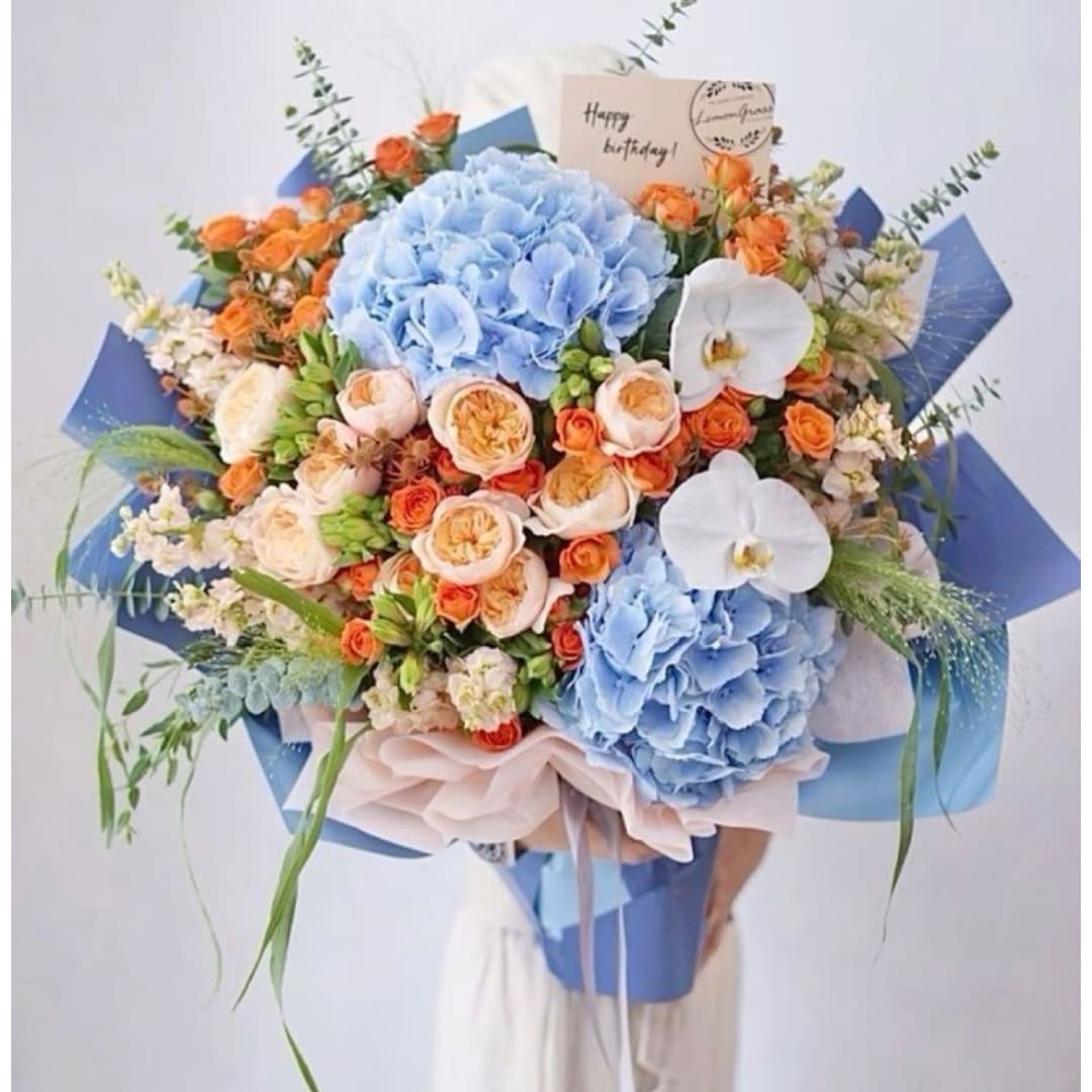 Bouquet of blue hydrangeas, orange roses, and white orchids with a birthday card