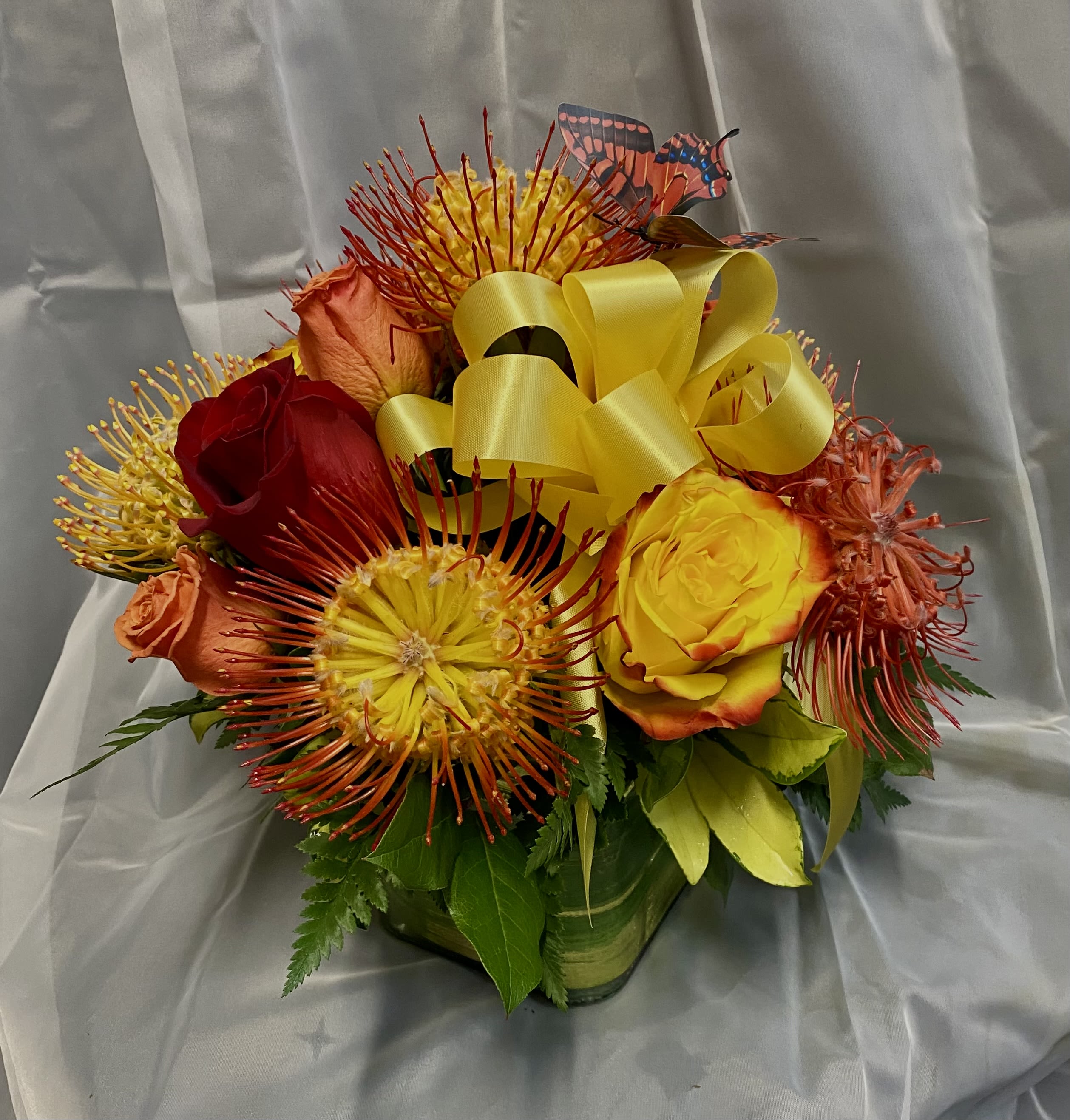 Bouquet of red, yellow, and orange roses with spiky blooms and a yellow ribbon