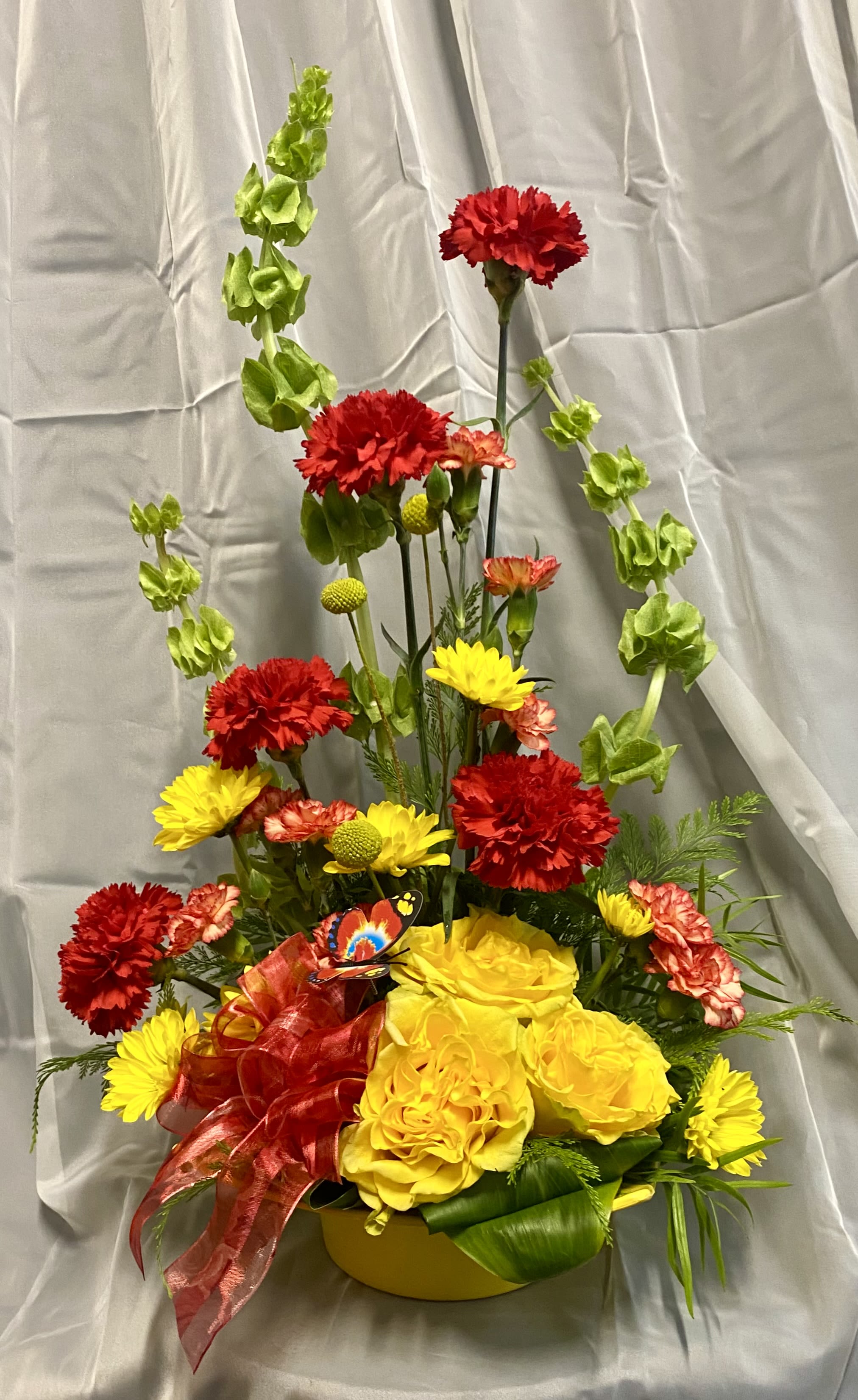 Yellow and red floral arrangement in a round container with a red ribbon