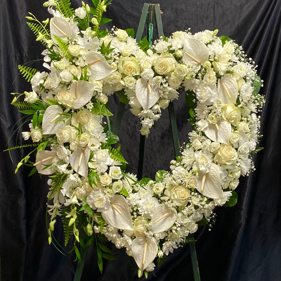 Heart-shaped white floral wreath on a stand with roses and anthuriums