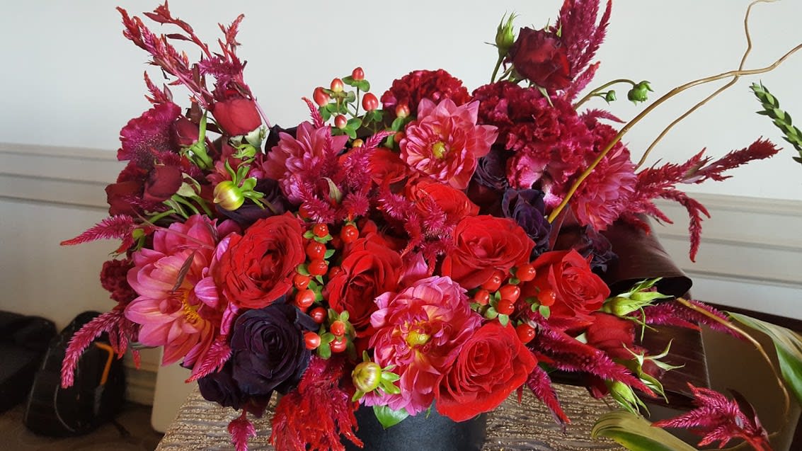 Lush arrangement of red and pink roses and dahlias in a black cylinder vase
