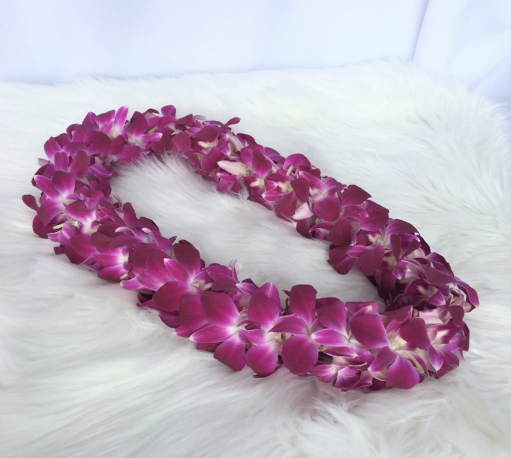Purple orchid flower lei arranged in an oval on a white fur surface