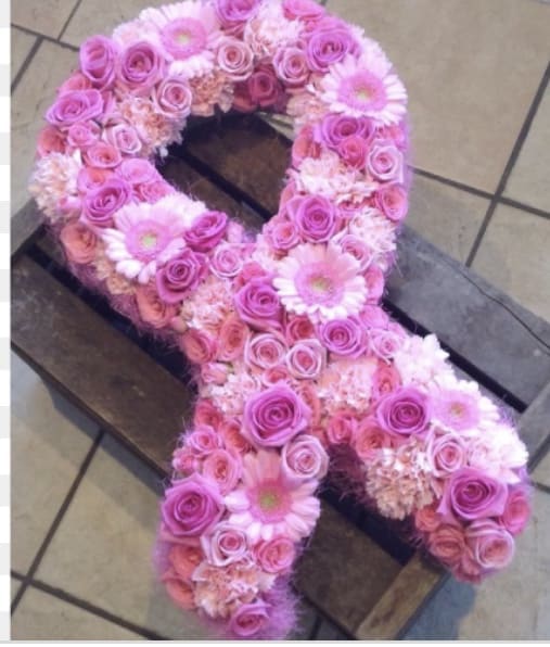 Pink floral arrangement shaped like an awareness ribbon on a wooden crate