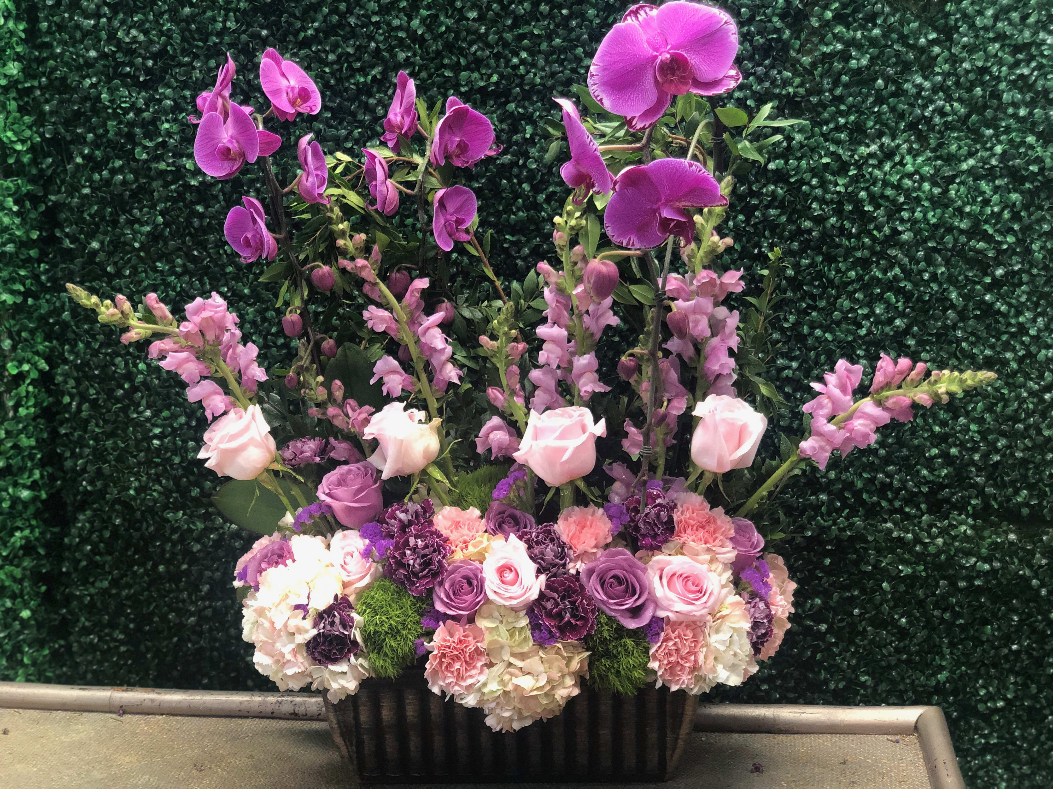 Tall floral arrangement with pink orchids, roses, and snapdragons in a black container