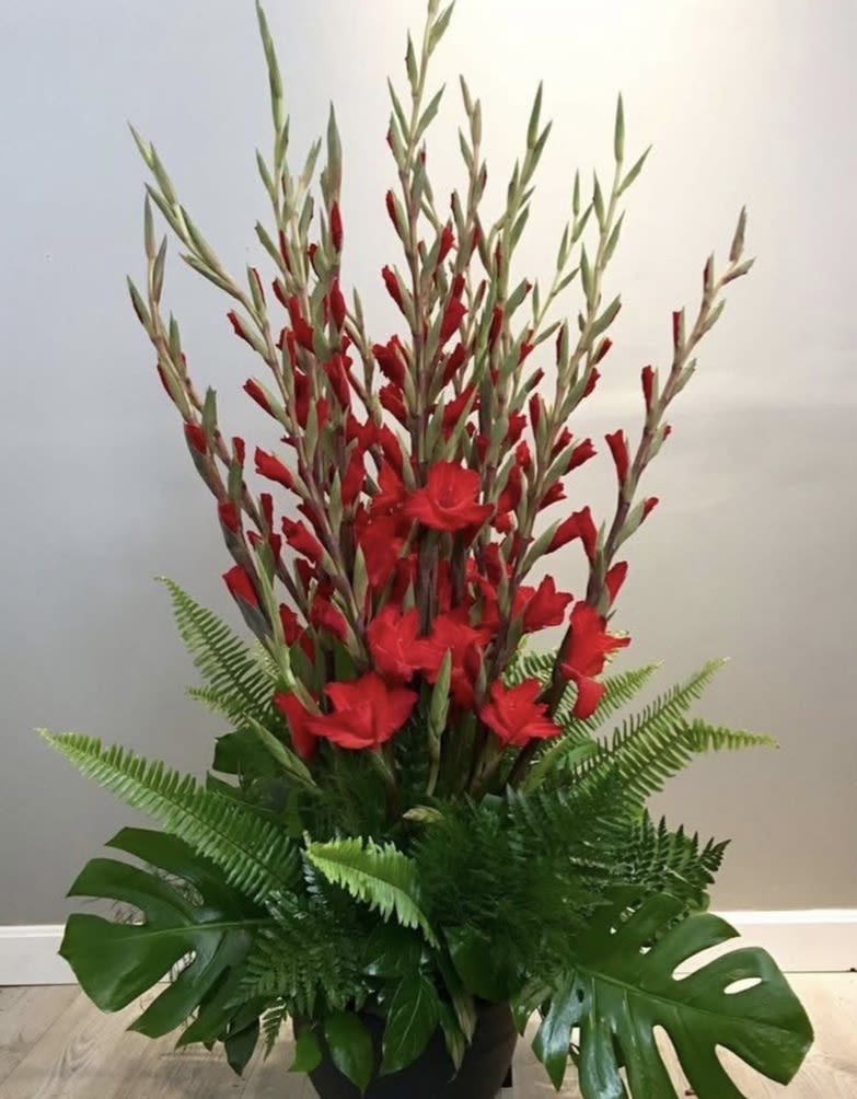 Tall red floral arrangement with tropical greenery in a black container