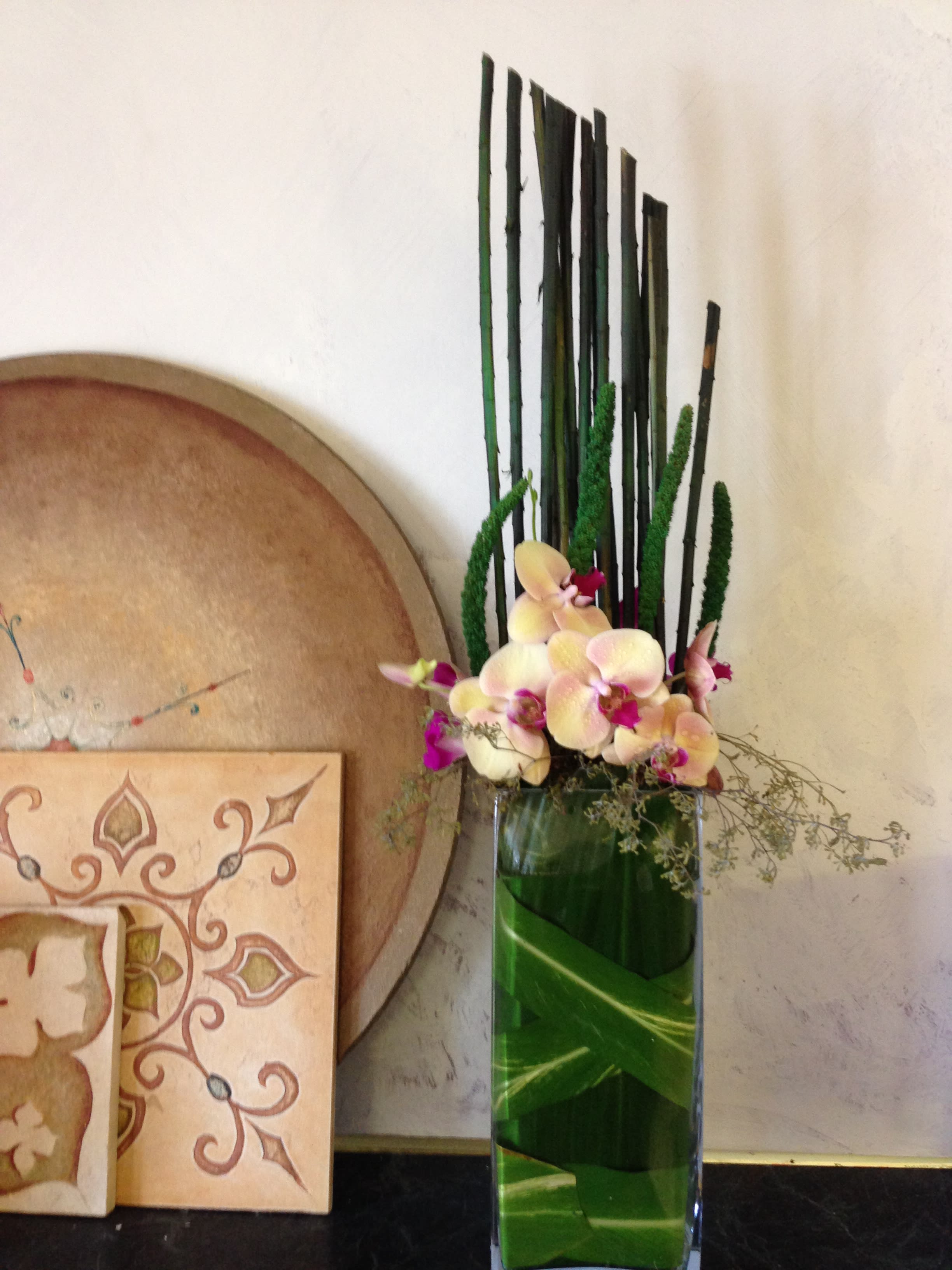 Tall orchid arrangement in a glass vase with dark decorative reeds