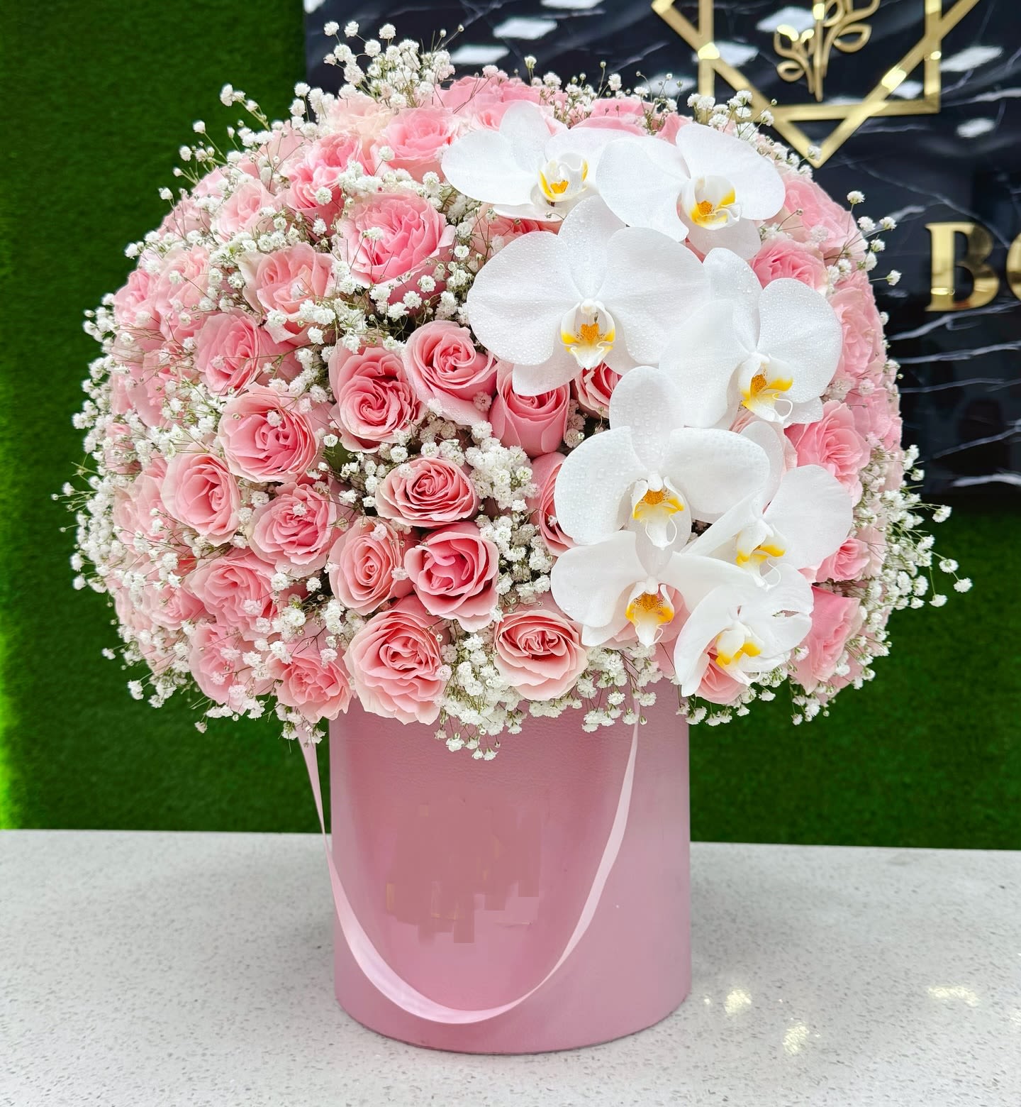 Pink roses and white orchids arranged in a pink hatbox