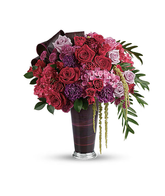 Cascading Elegance Bouquet - A dramatic display in jewel-toned roses and hydrangea in a sophisticated vase, this majestic bouquet will take their breath away. Dark pink hydrangea, lavender hydrangea, lavender roses, light lavender roses, red roses, red spray roses, purple carnations, purple button spray chrysanthemums, and purple cushion spray chrysanthemums are arranged with hanging green amaranthus, israeli ruscus, xanadu philodendron leaves, and red ti leaves. Delivered in a glass romanesque vase.