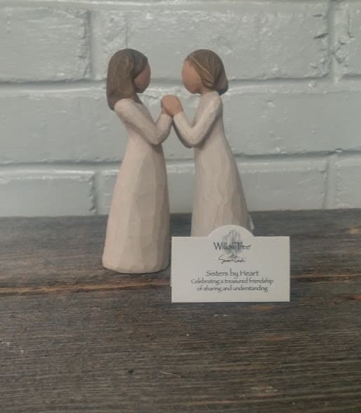 Two small figurines of girls facing each other and holding hands