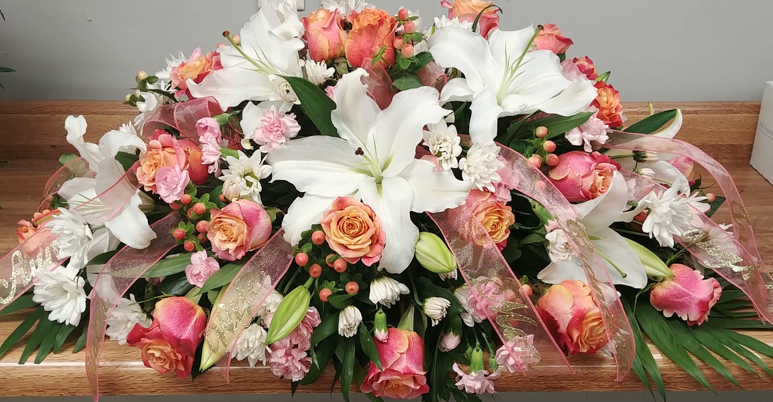Large floral casket spray with white lilies, pink roses, and ribbon accents