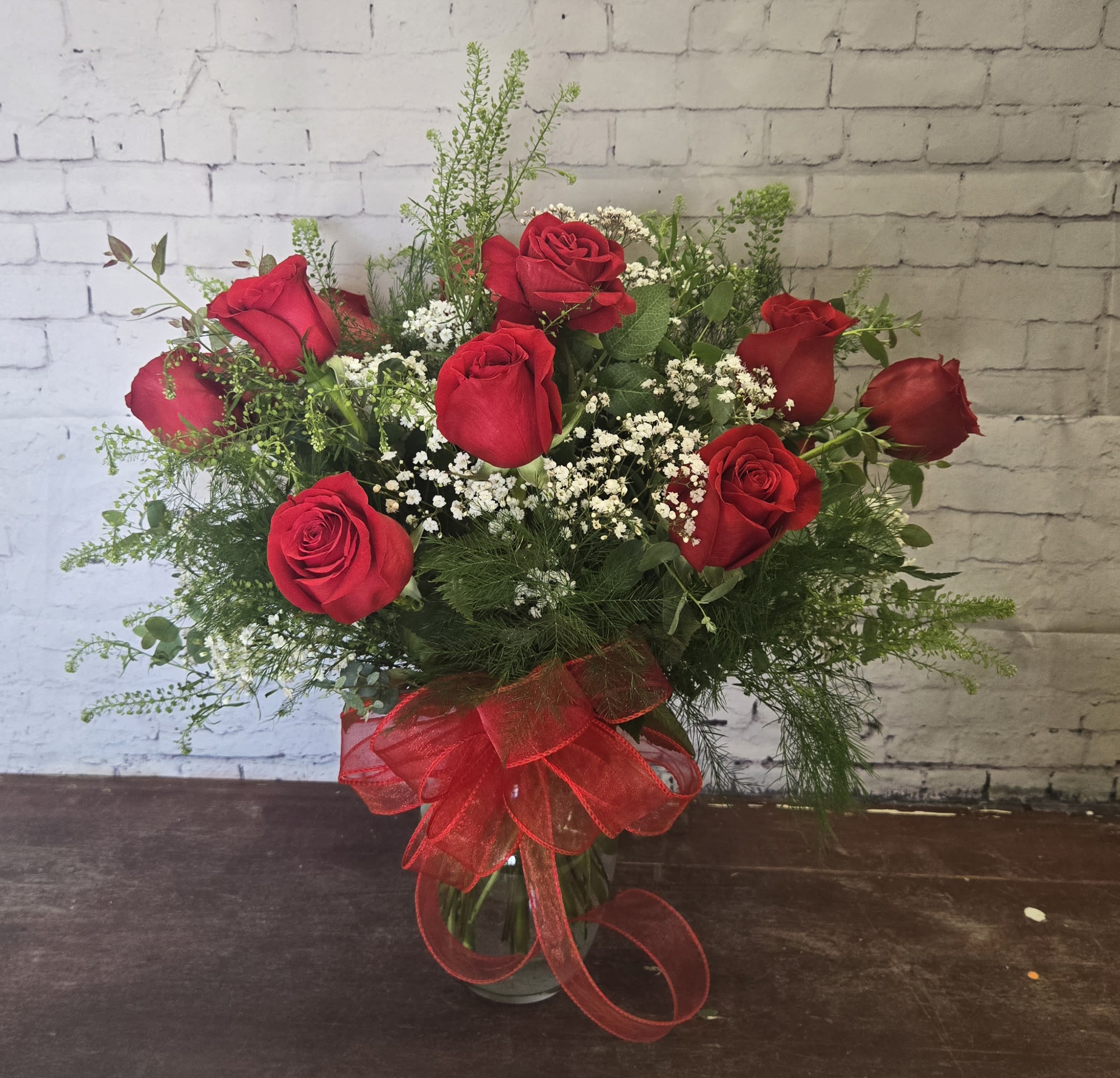 Red roses arranged in a glass vase with baby's breath and a red ribbon
