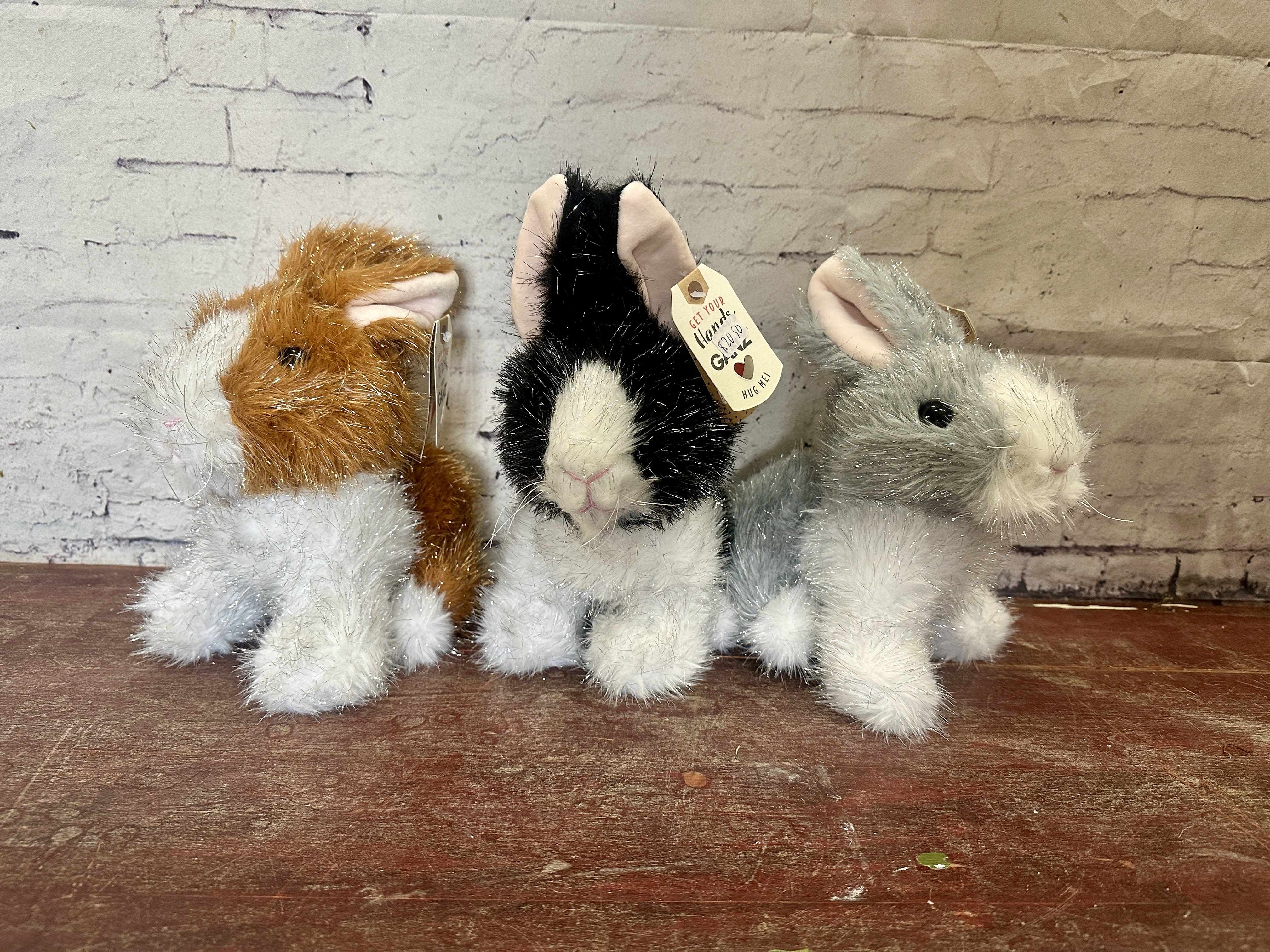 Three plush bunny figurines sit on a wooden surface.