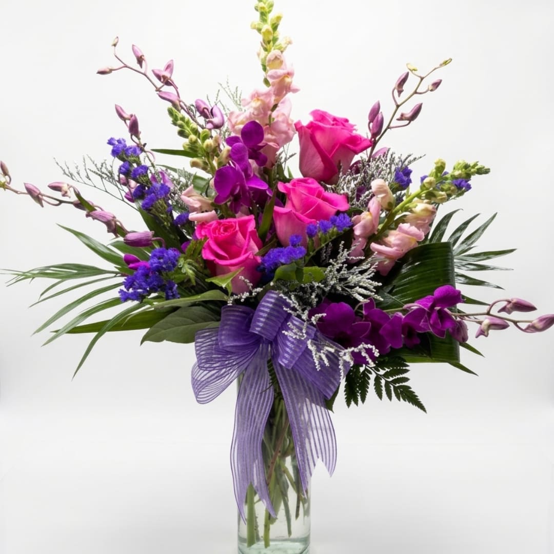Pink roses and purple orchids in a glass vase with a purple ribbon