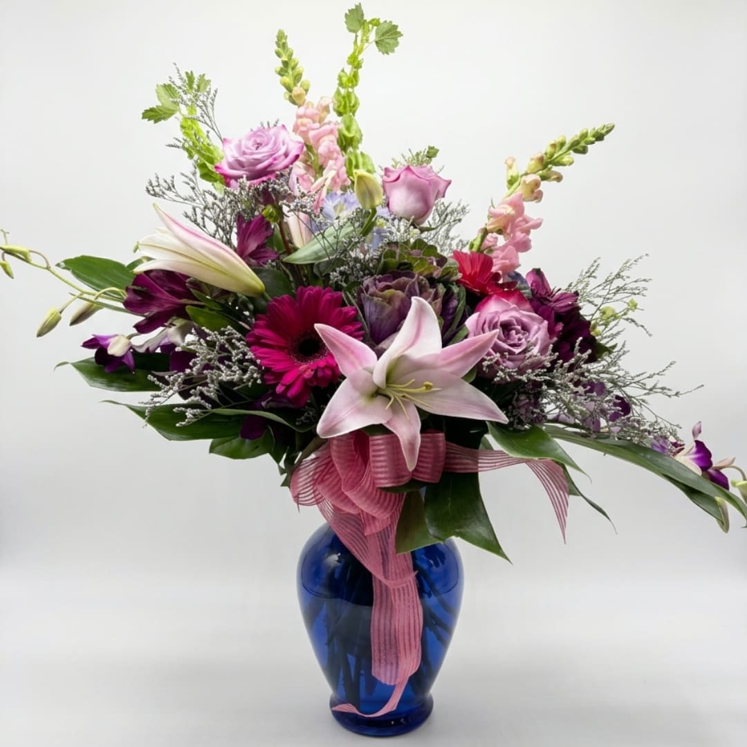 Pink and purple mixed bouquet in a blue glass vase with a ribbon
