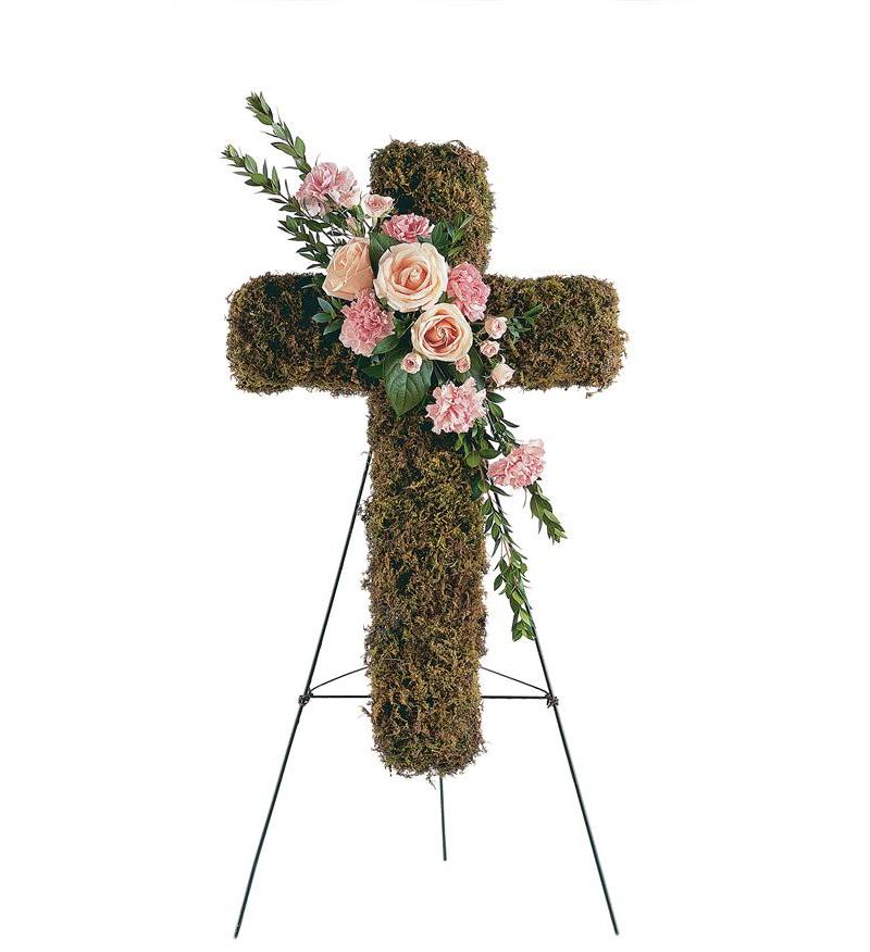Moss-covered cross with pink roses and carnations on a stand
