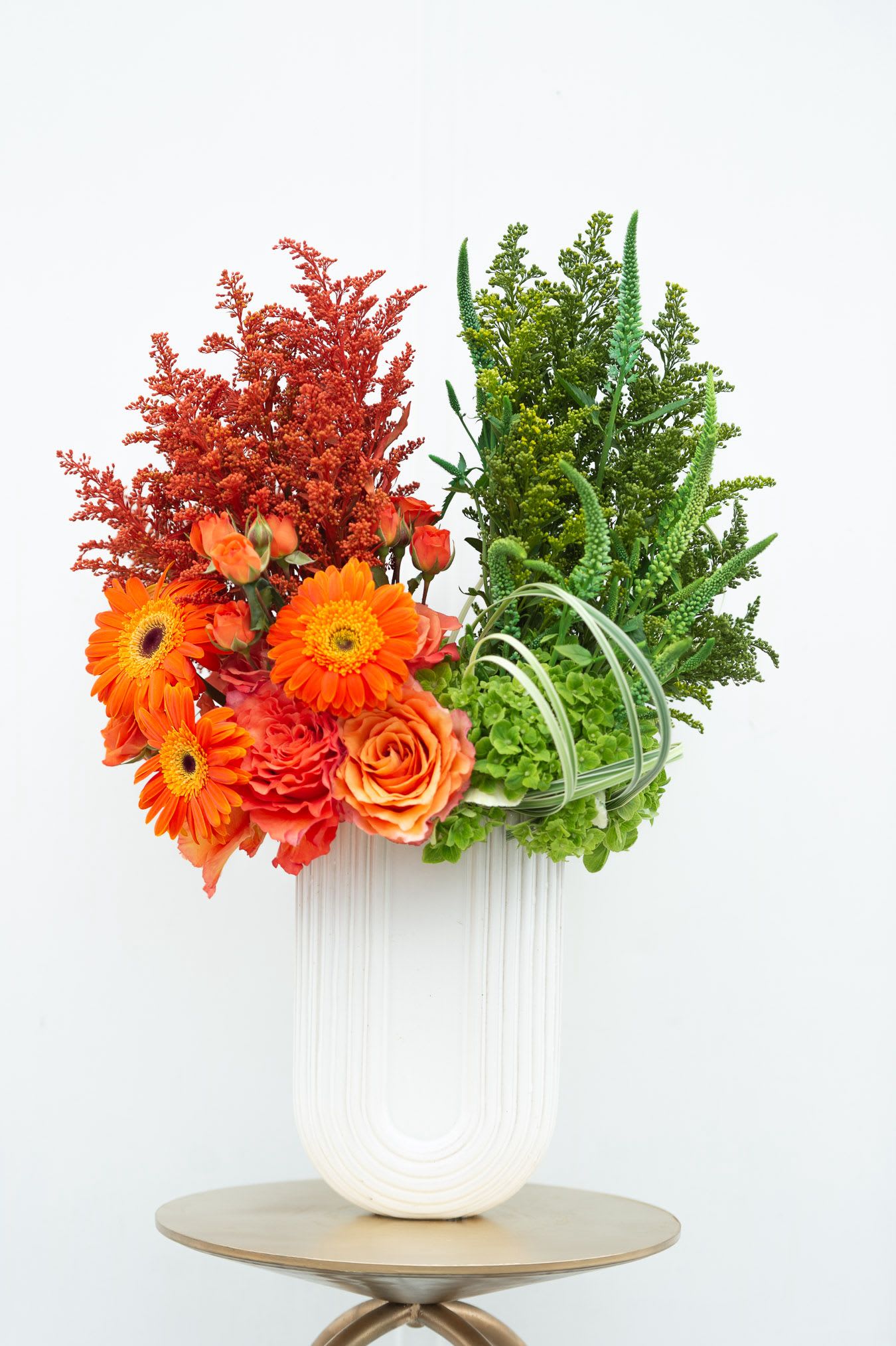 Orange flowers and green foliage arranged in a white vase