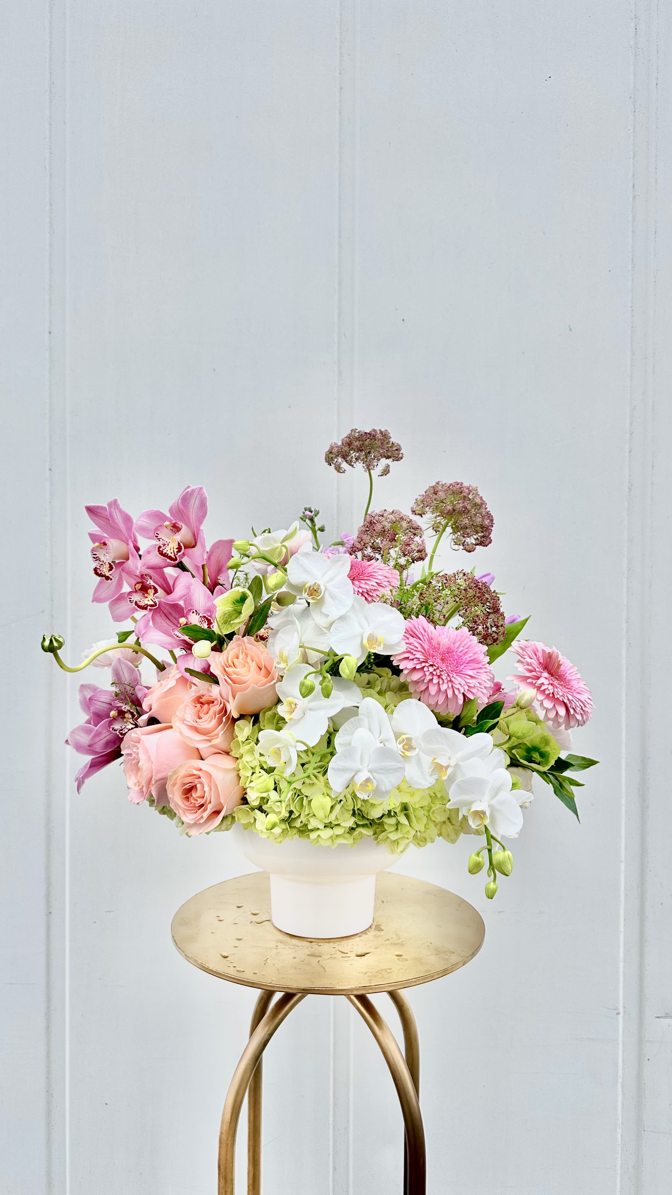 Mom's Favorite - Lush, vibrant, and undeniably elegant, Mom’s Favorite is a show-stopping arrangement designed to make her feel truly cherished. Featuring striking pink orchids as the centerpiece, this design is layered with soft green hydrangea, delicate tulips, and creamy white roses for a look that’s both modern and timeless.  Artfully arranged in a sleek ceramic vessel, this piece brings together bold beauty and graceful movement, creating a fresh-from-the-garden feel with a refined finish.  Perfect for the mom who loves something a little extra special, Mom’s Favorite is a stunning way to celebrate her with beauty, love, and appreciation this Mother’s Day.