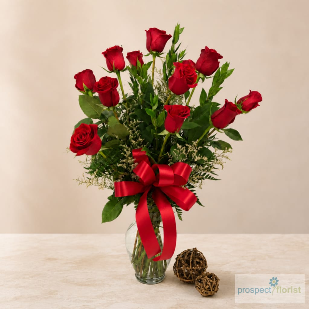 Red roses arranged in a clear glass vase with a red ribbon