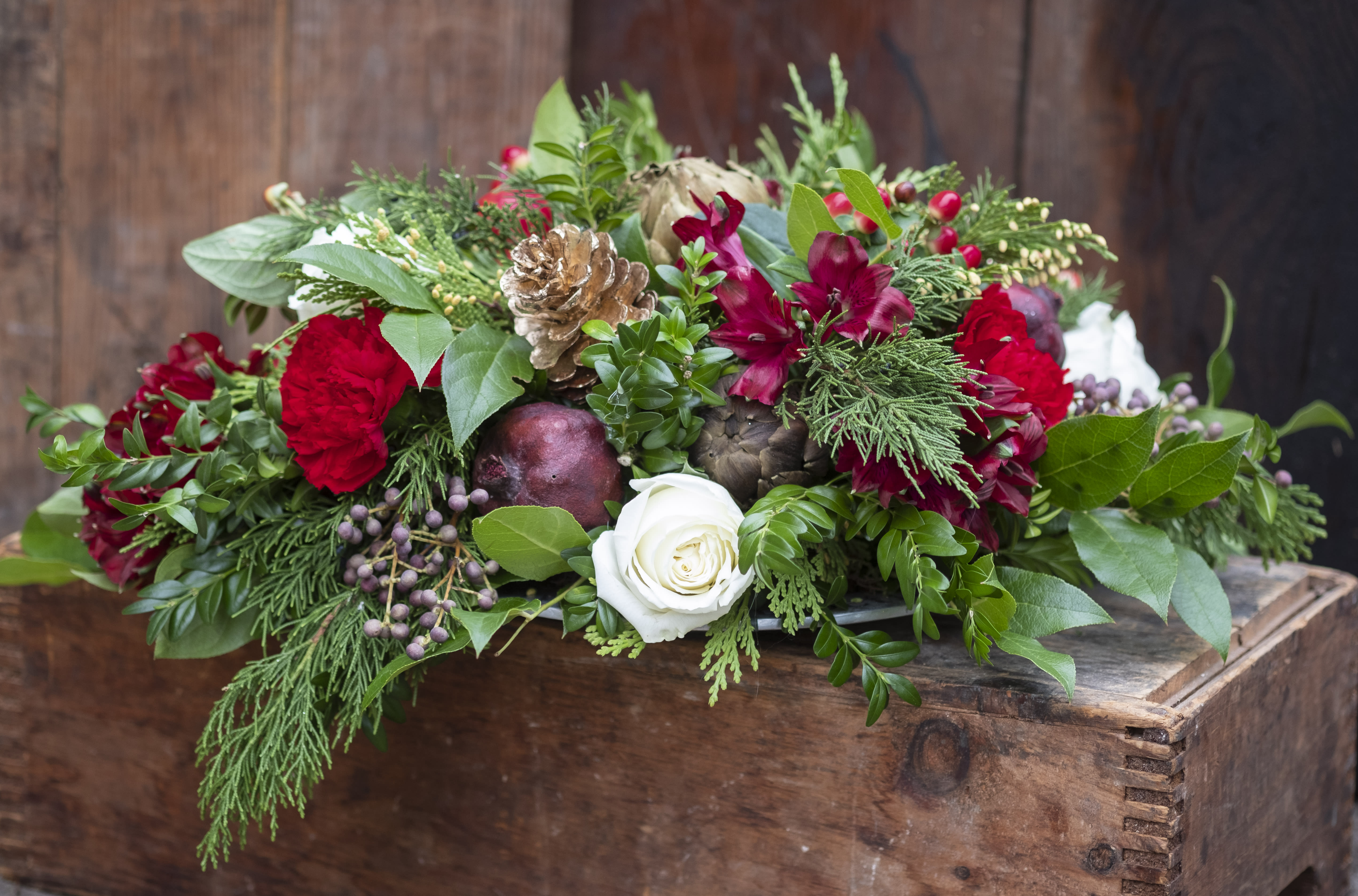Holiday floral arrangement with red blooms and a white rose in a wooden box