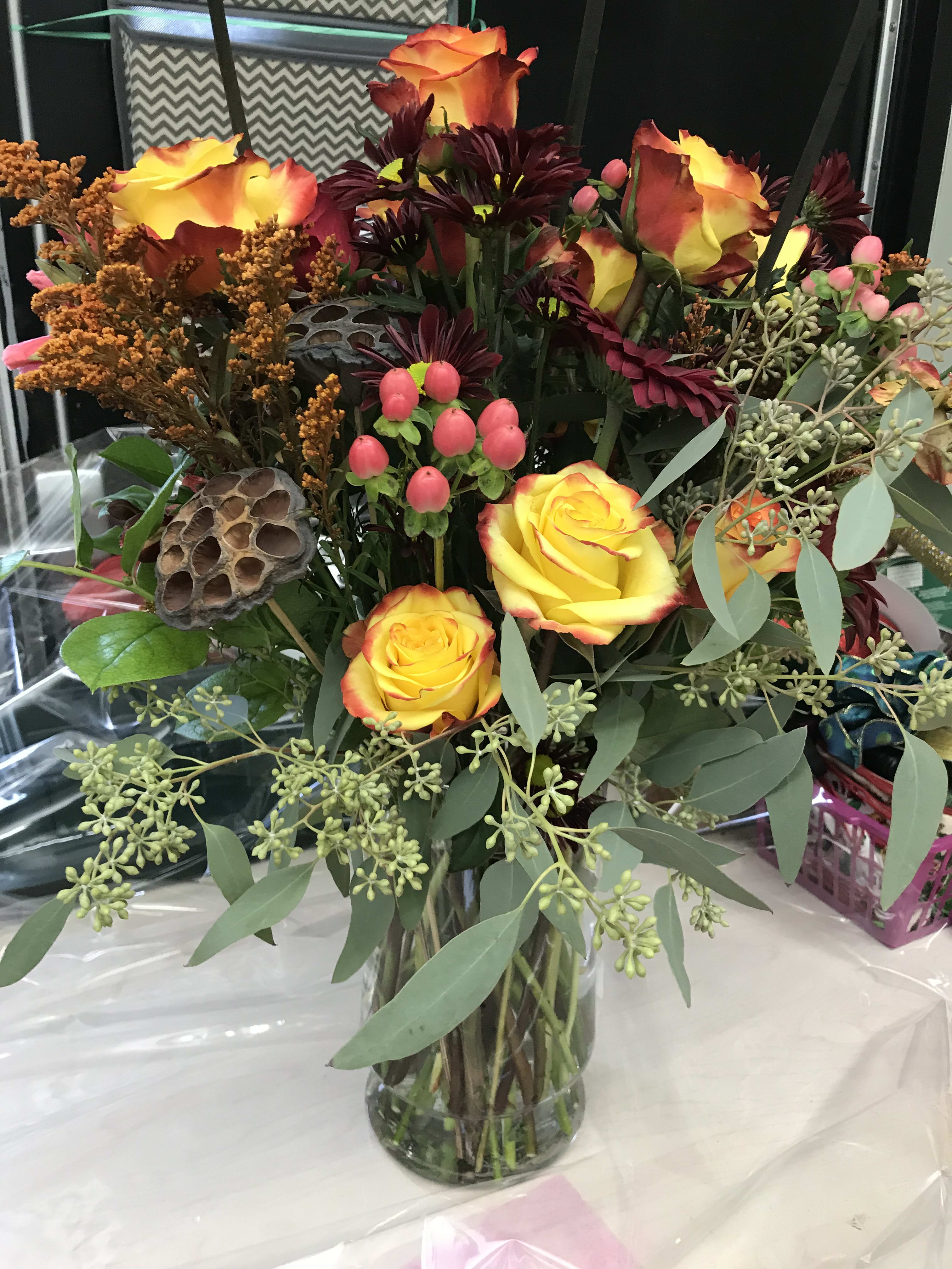 Bouquet of yellow-orange roses in a glass vase with burgundy flowers