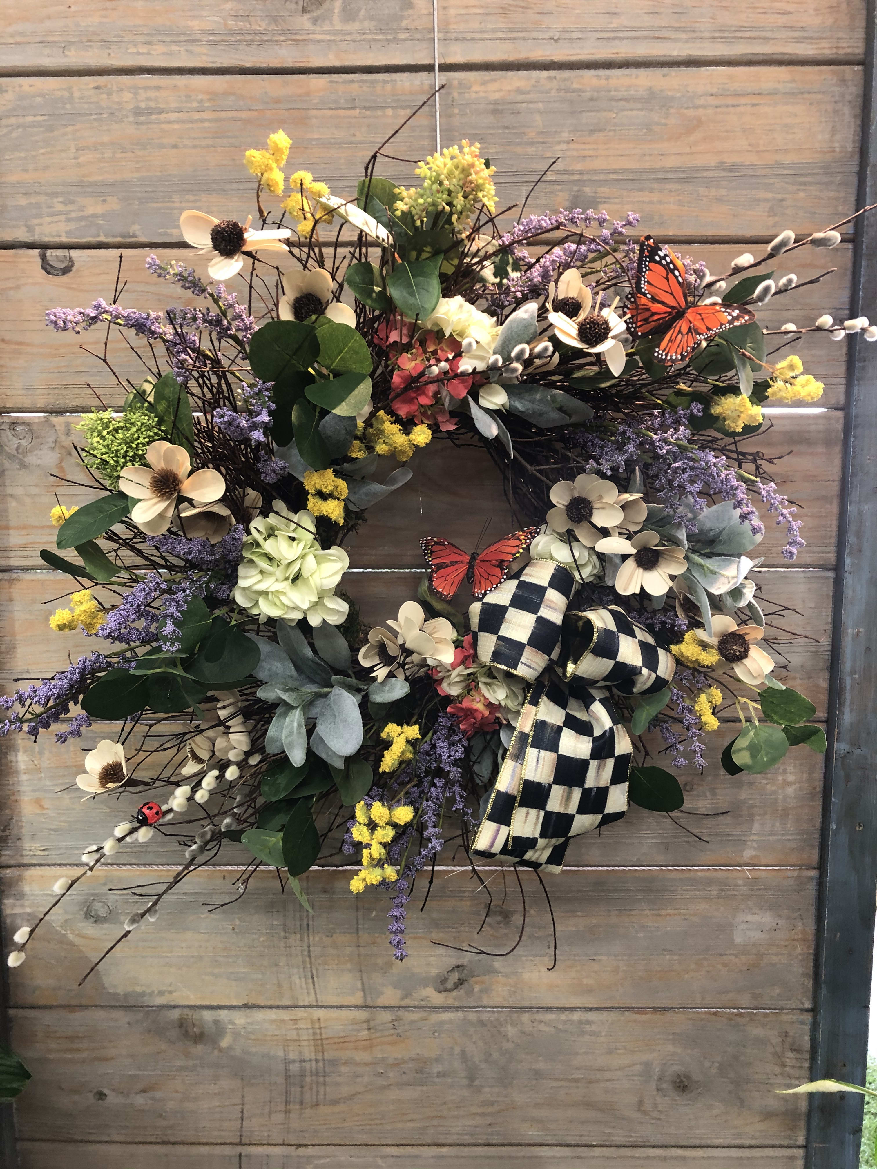 Floral wreath with cream flowers, purple accents, and a checkered bow