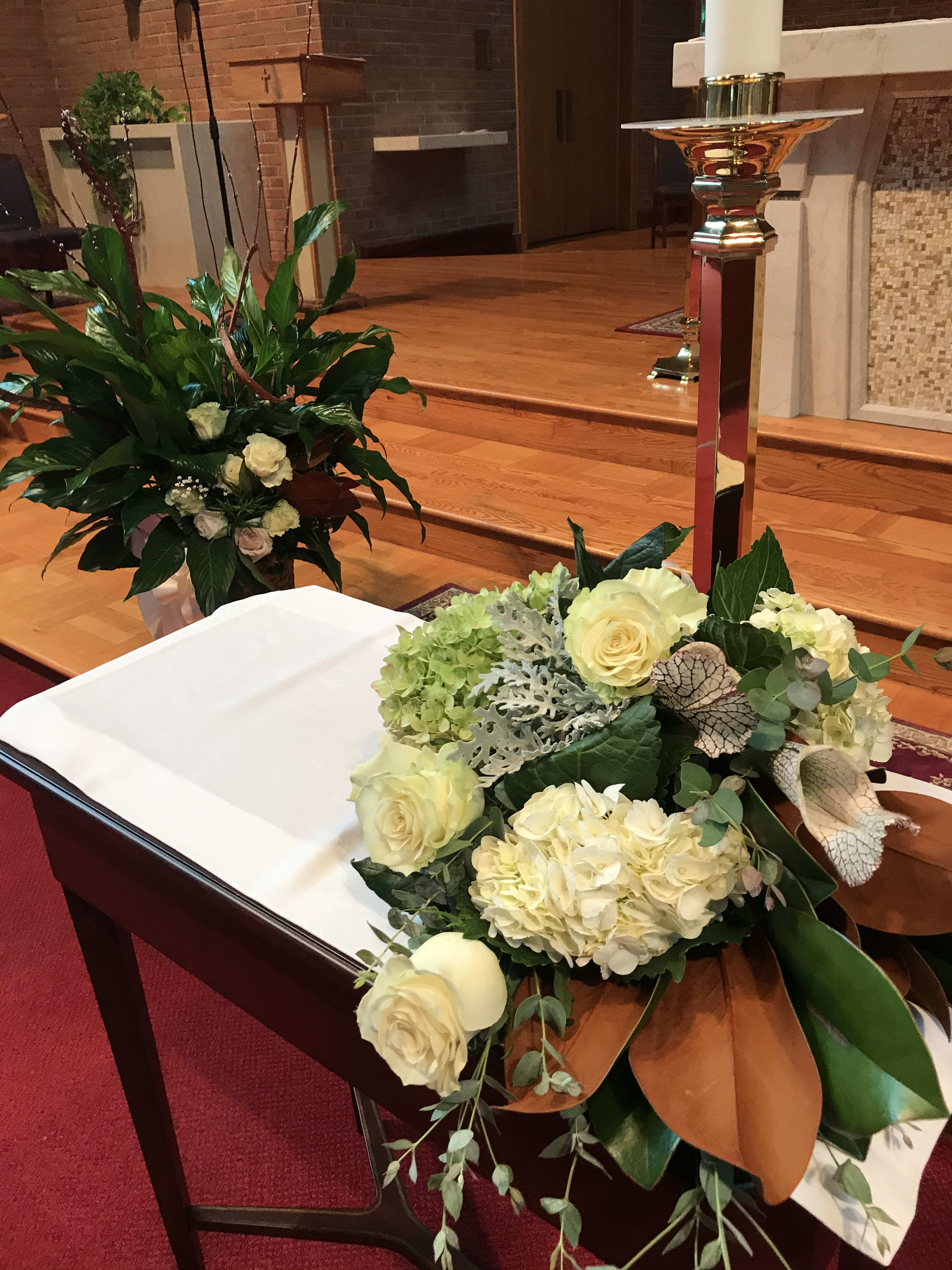 Cream floral arrangement on a church altar beside a white-draped casket