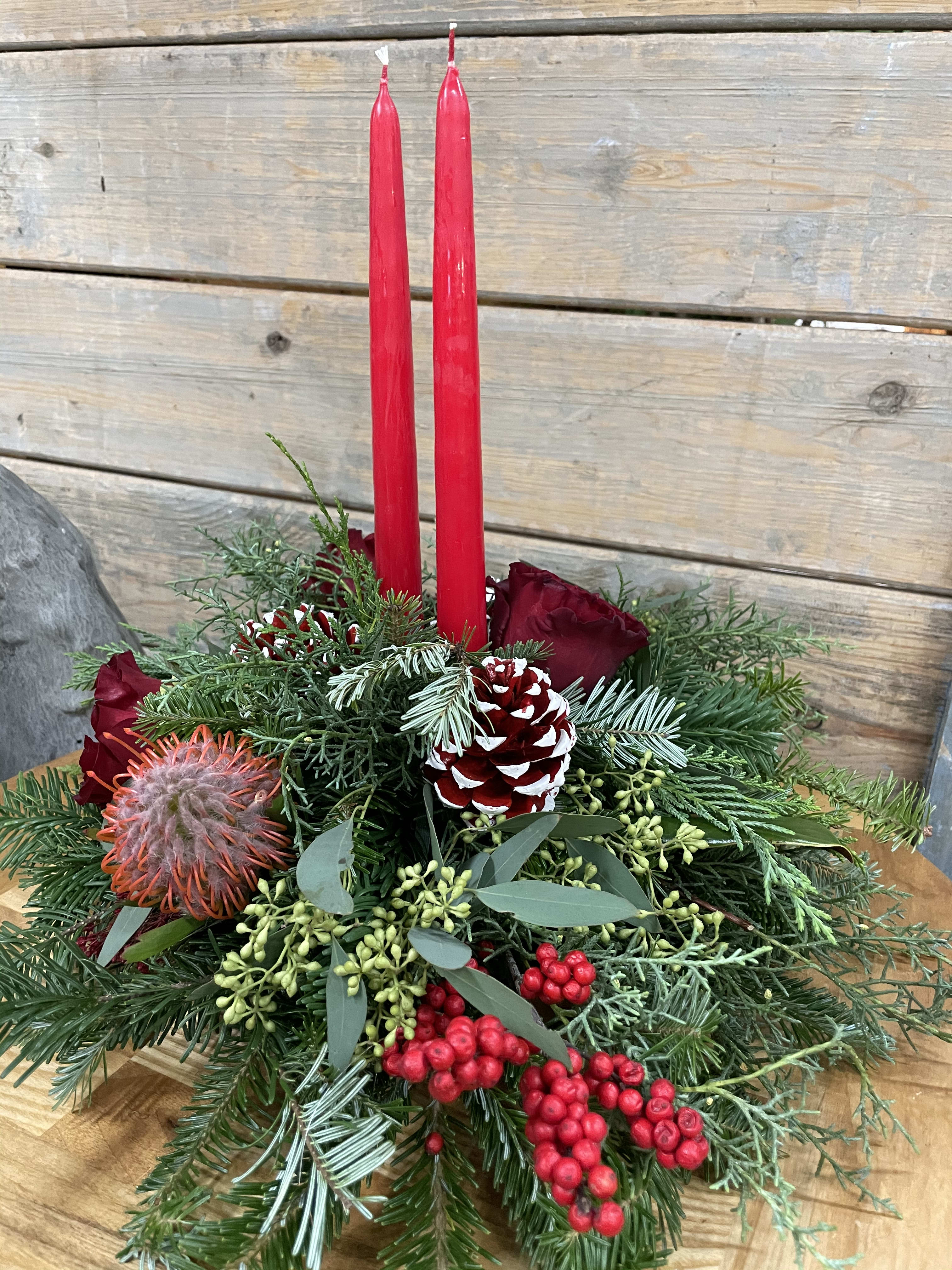 Holiday centerpiece with red candles, roses, pinecones, and evergreen branches