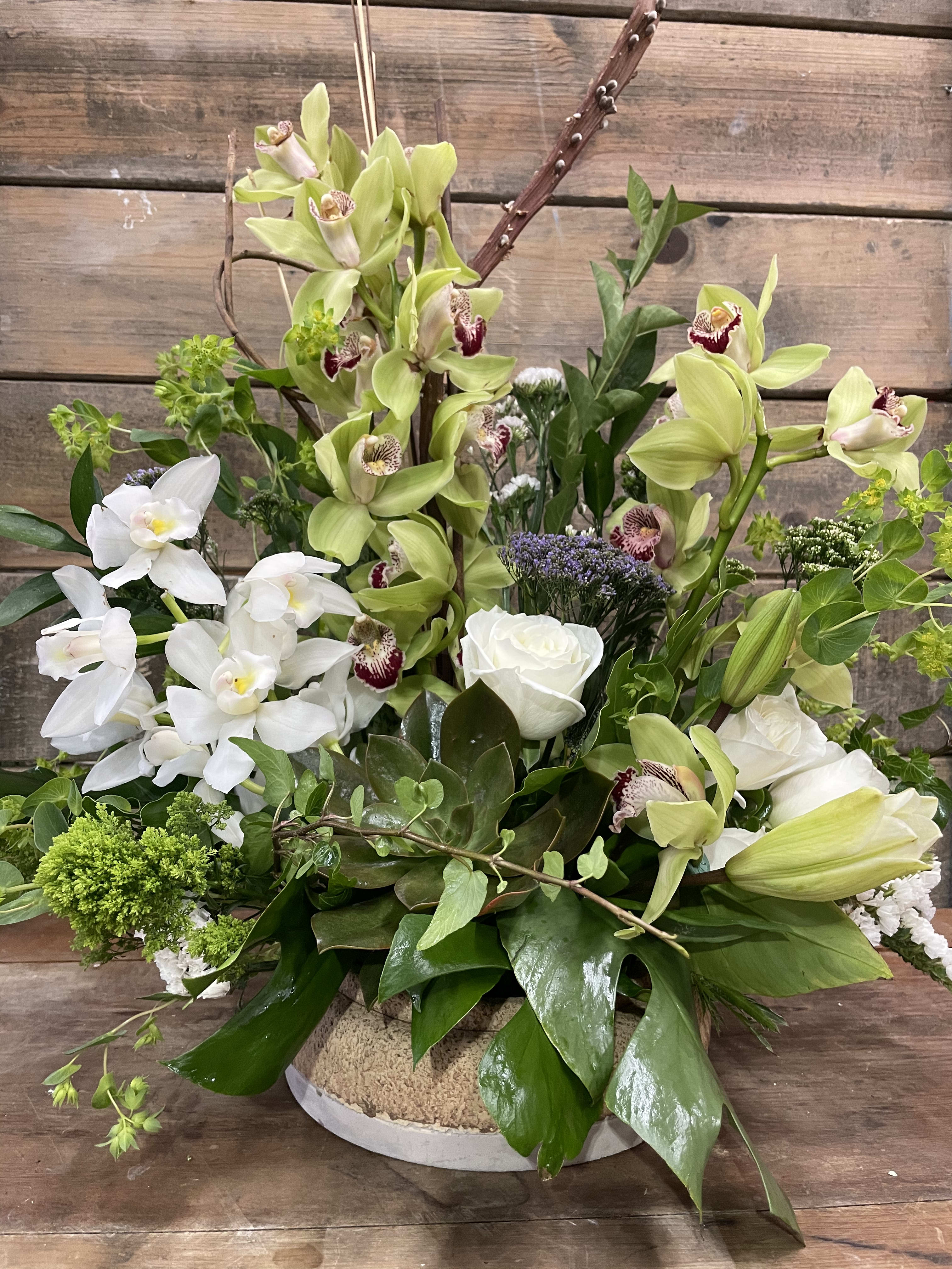 Mixed floral arrangement with white and green orchids and roses in a low container