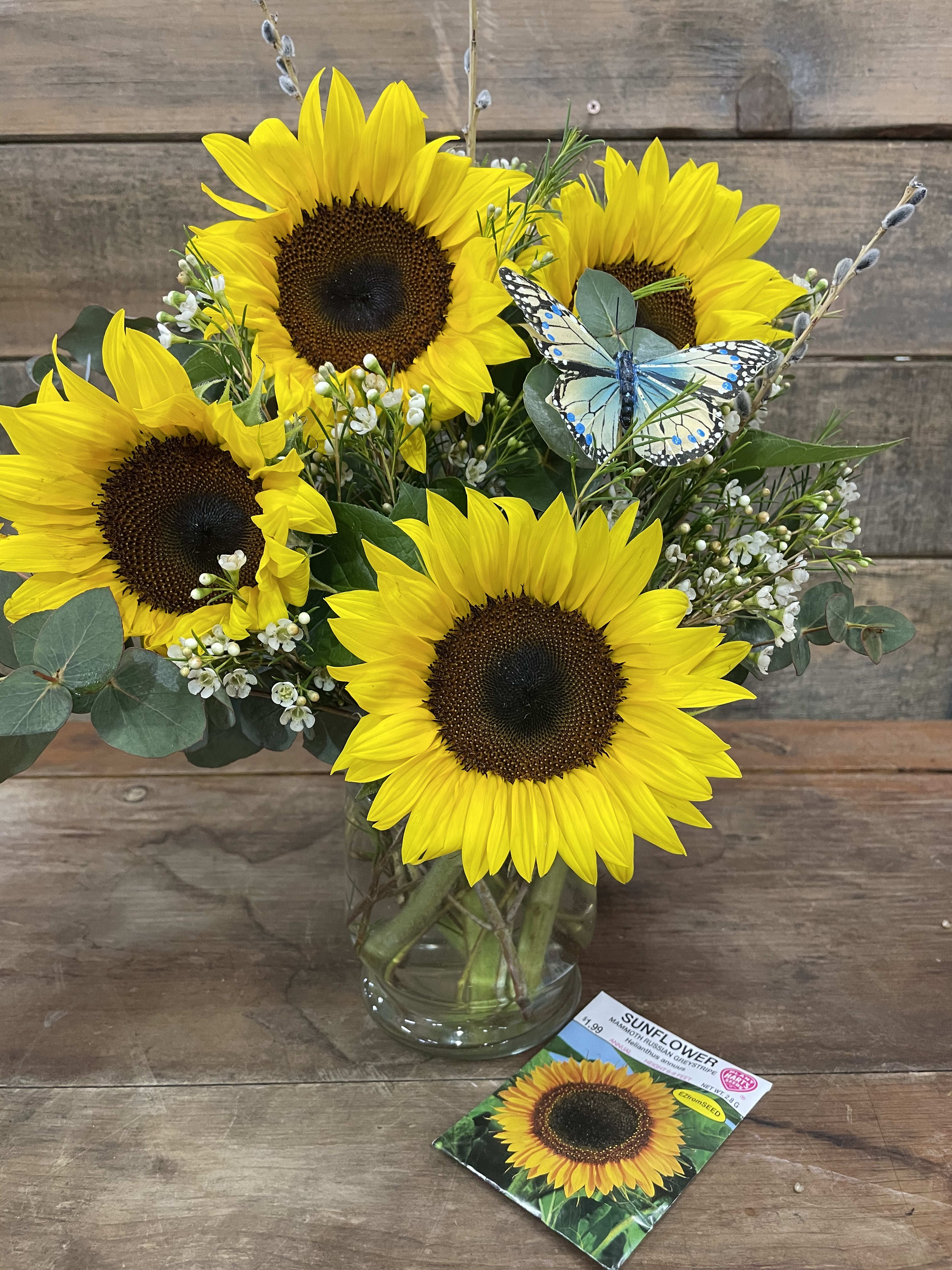 Sunflower bouquet in a glass vase with a butterfly pick