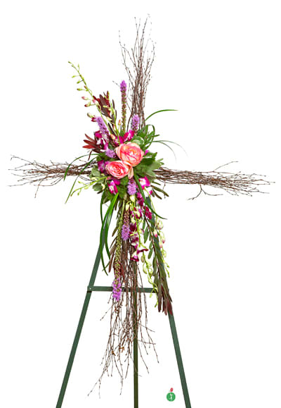 Standing twig cross with pink roses and purple flowers arranged on a green easel