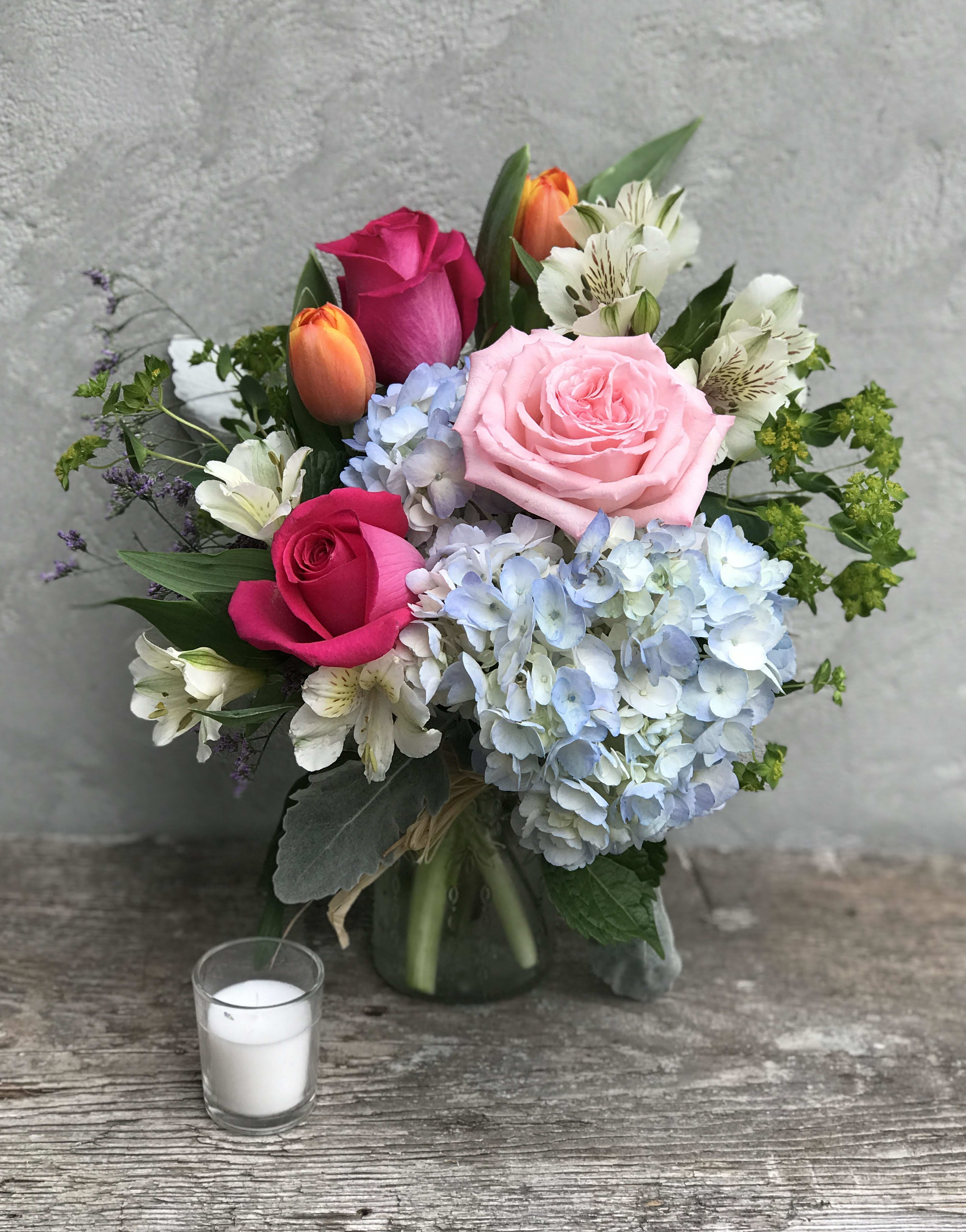 Bouquet of pink and orange roses with blue hydrangeas in a glass vase