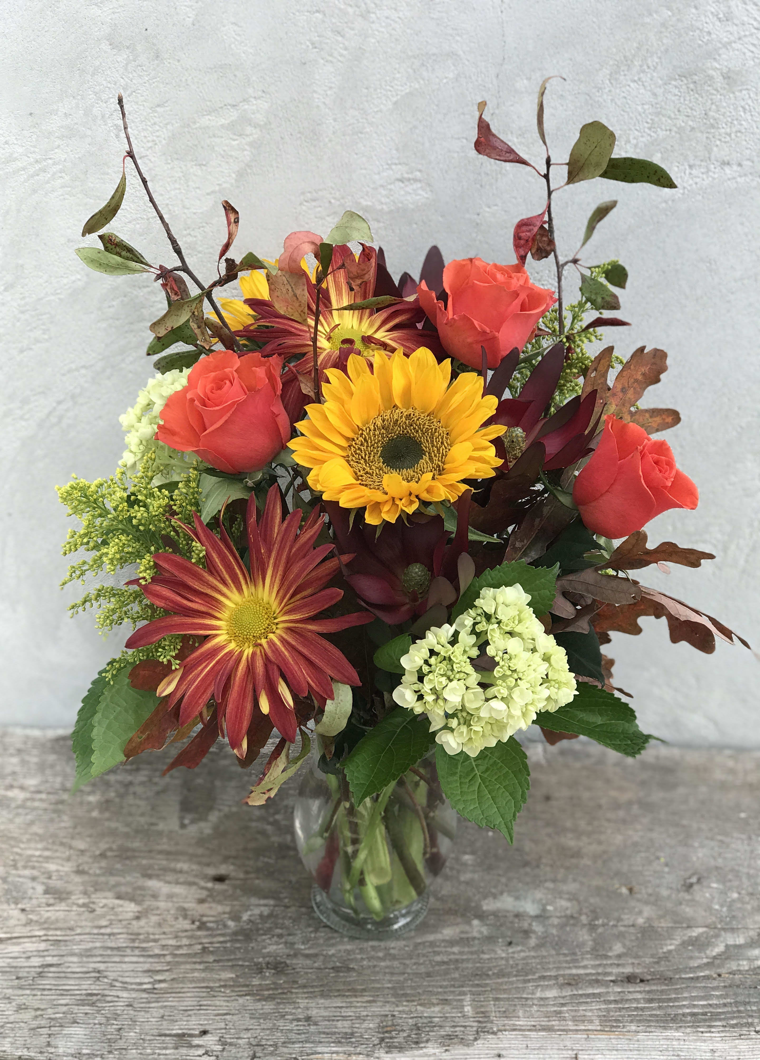 Mixed bouquet of roses, sunflowers, and chrysanthemums in a glass vase
