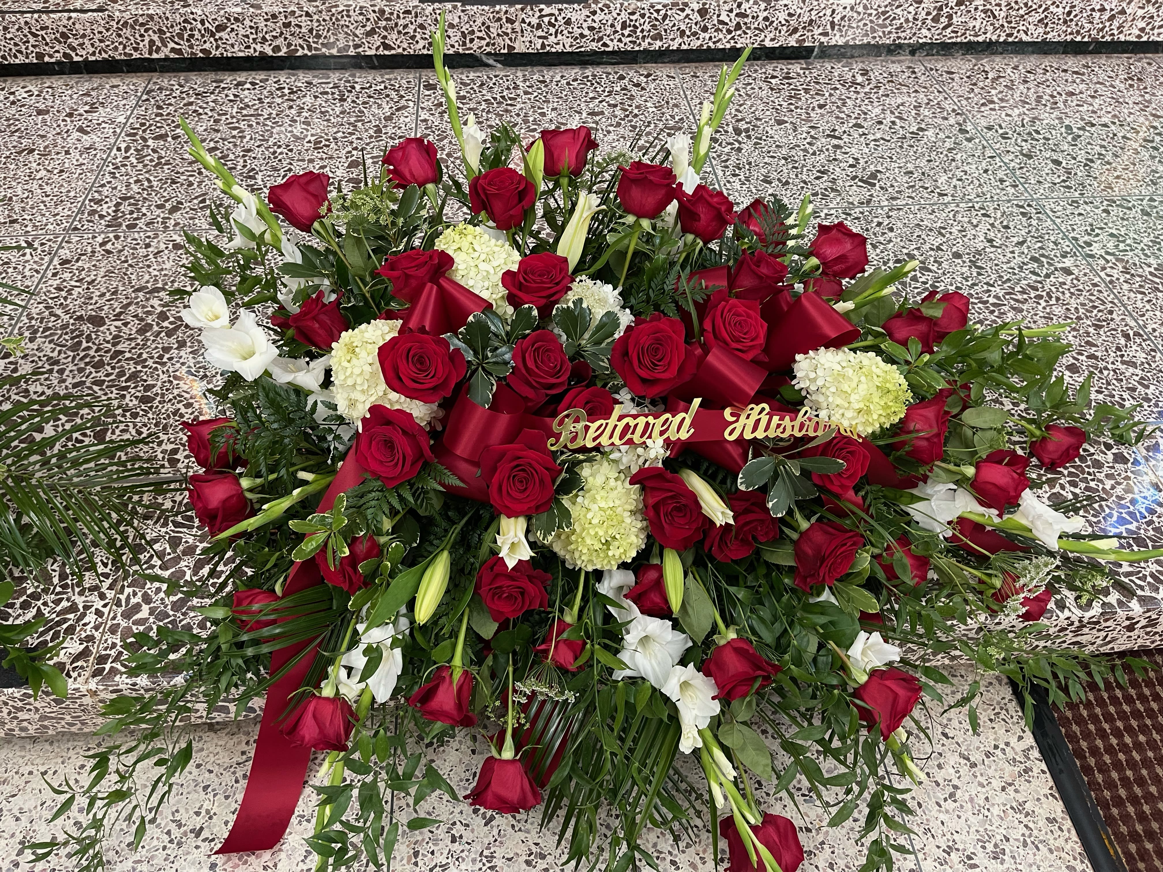 Large red and white floral funeral spray with ribbon and "Beloved Husband" sign