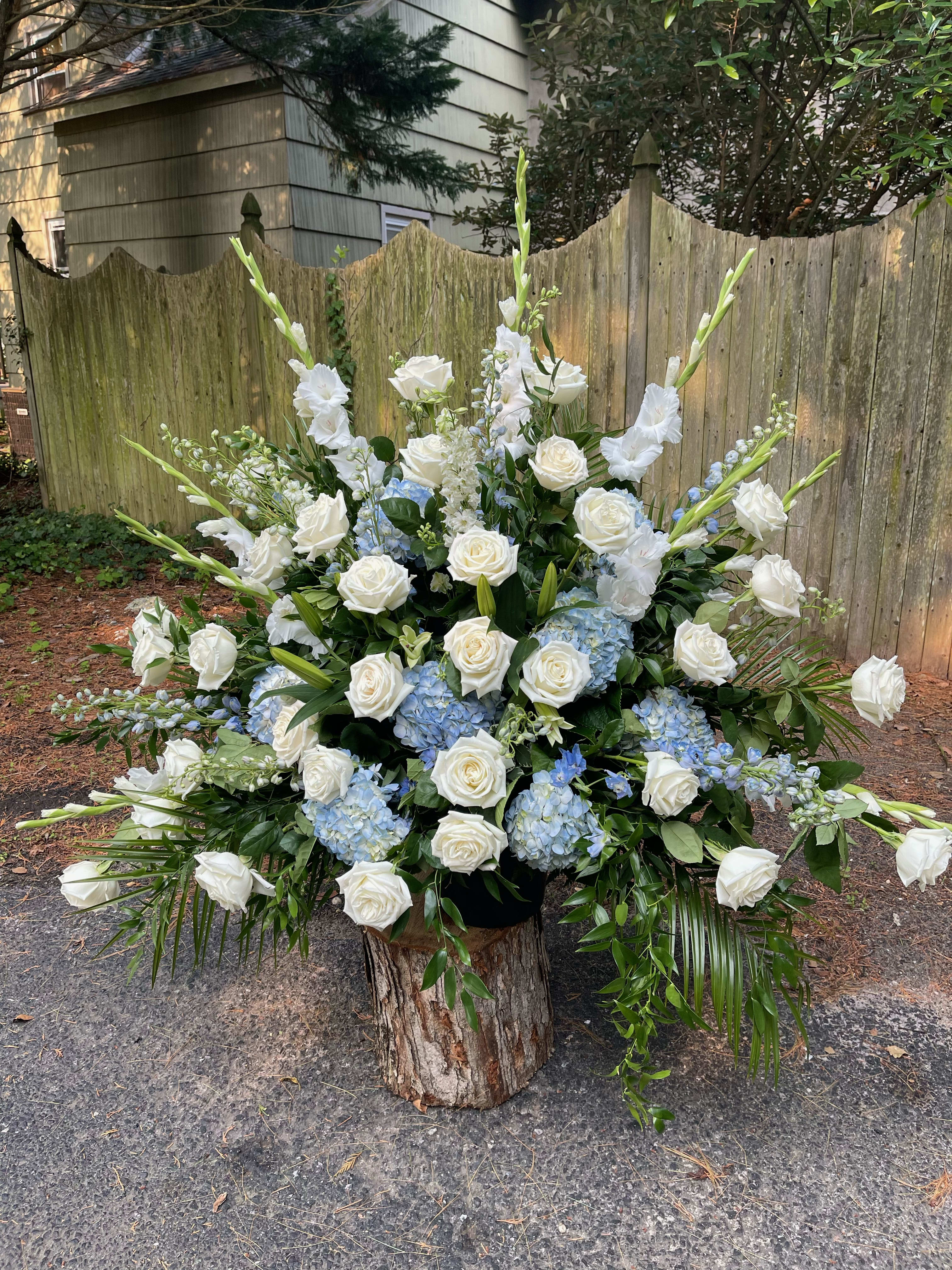 Large white and blue floral arrangement with roses and tall spikes in a wood base