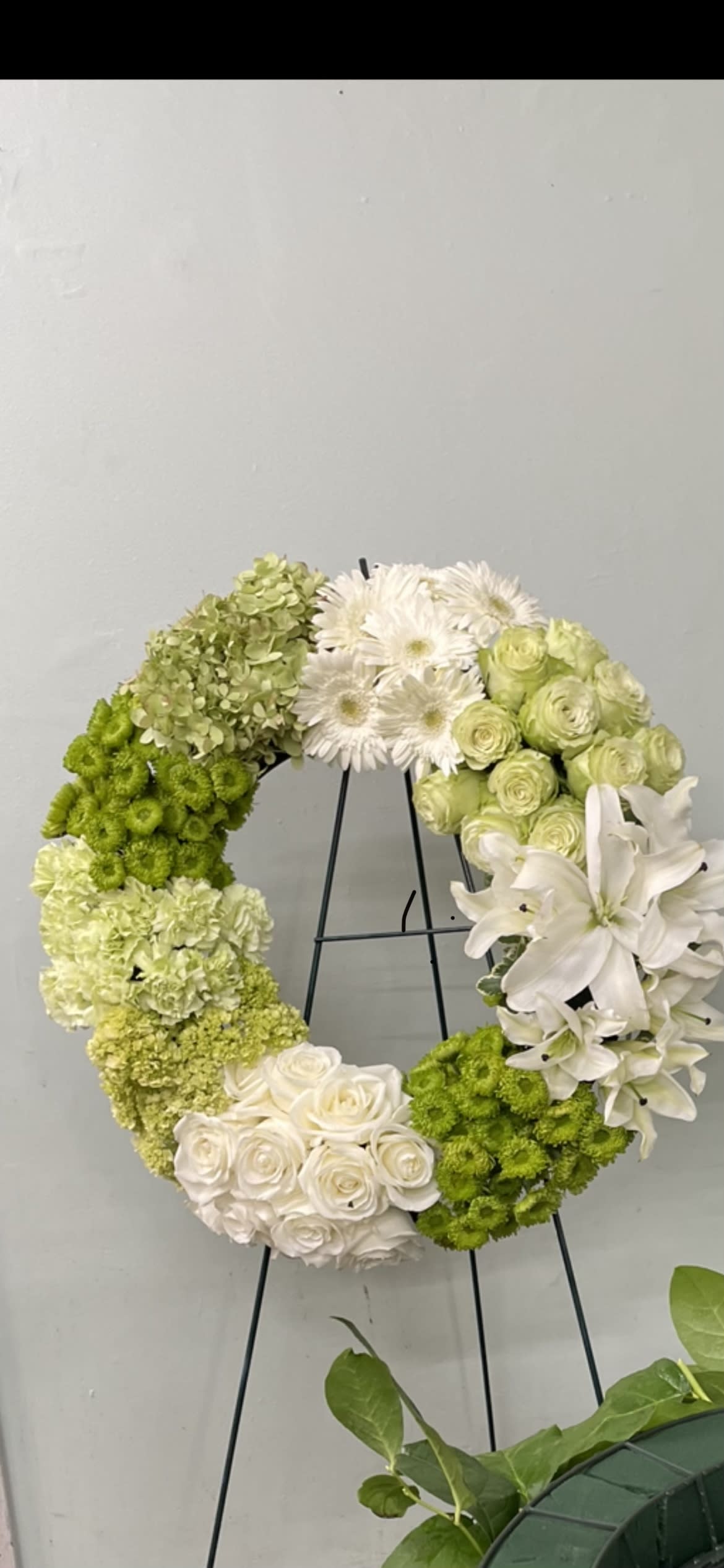 Circular floral wreath with white and green flowers on a black stand