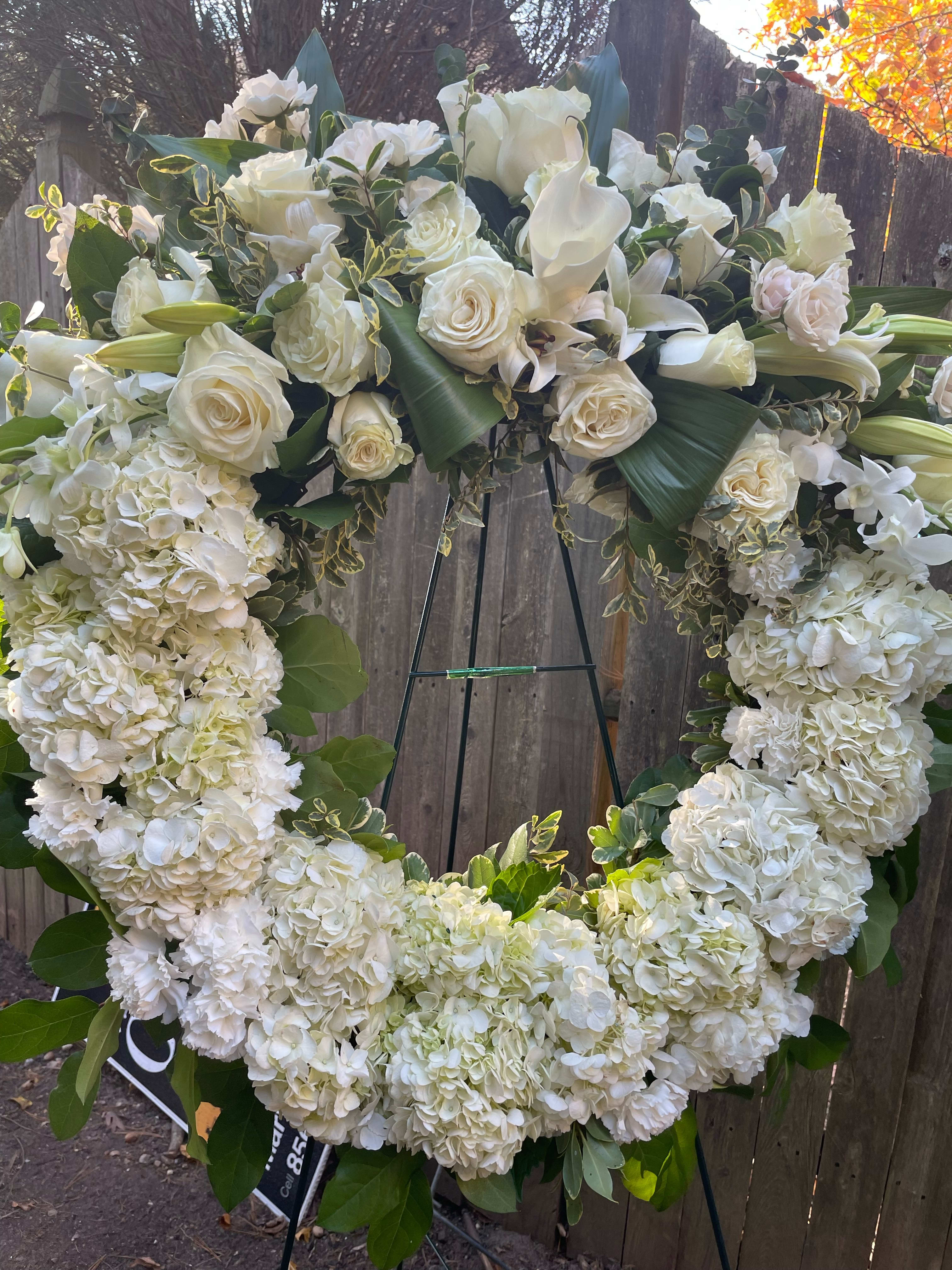 Large white floral wreath on an easel with roses, hydrangeas, and calla lilies