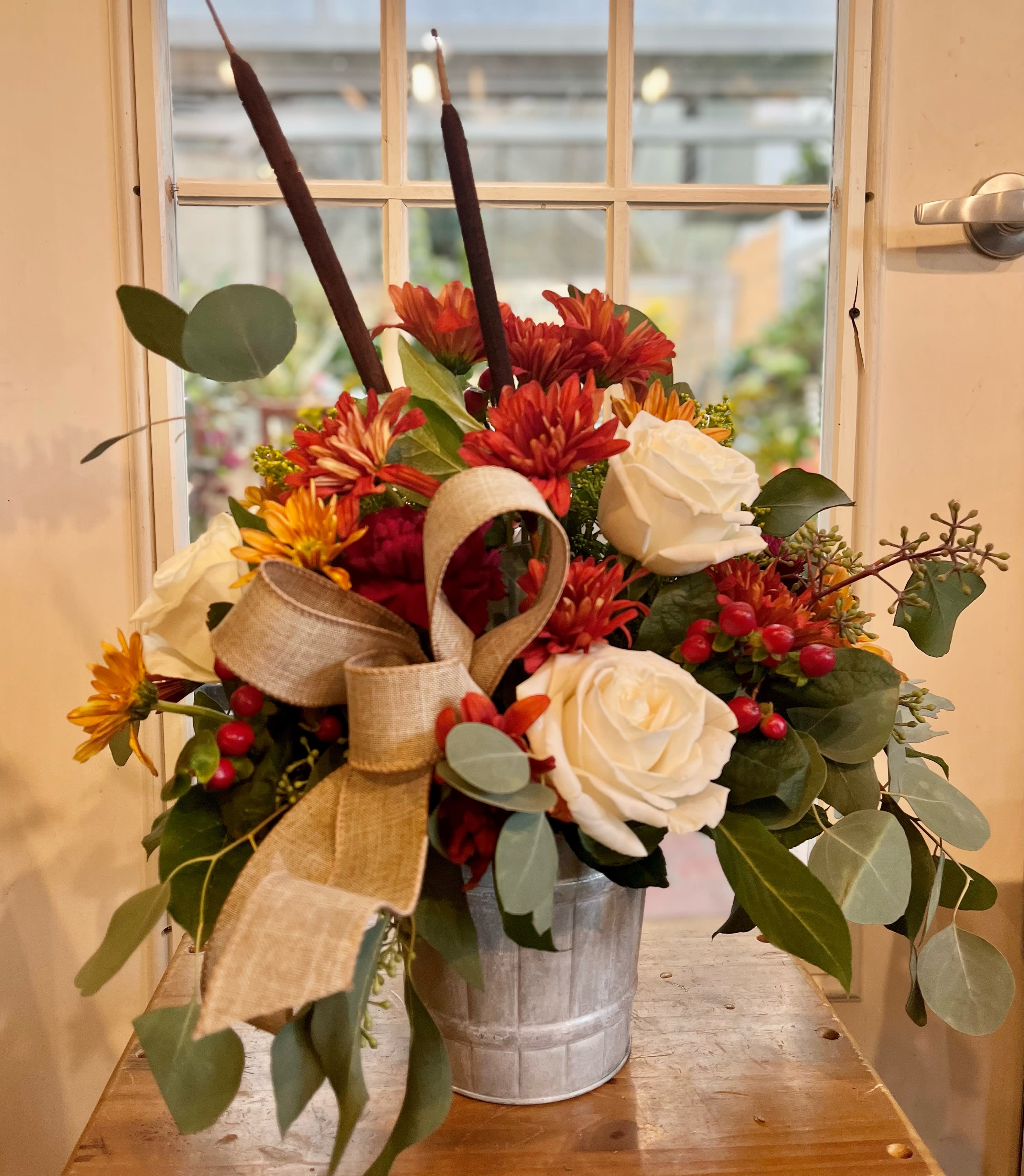 Bouquet of white roses and red-orange mums in a metal bucket with a burlap bow