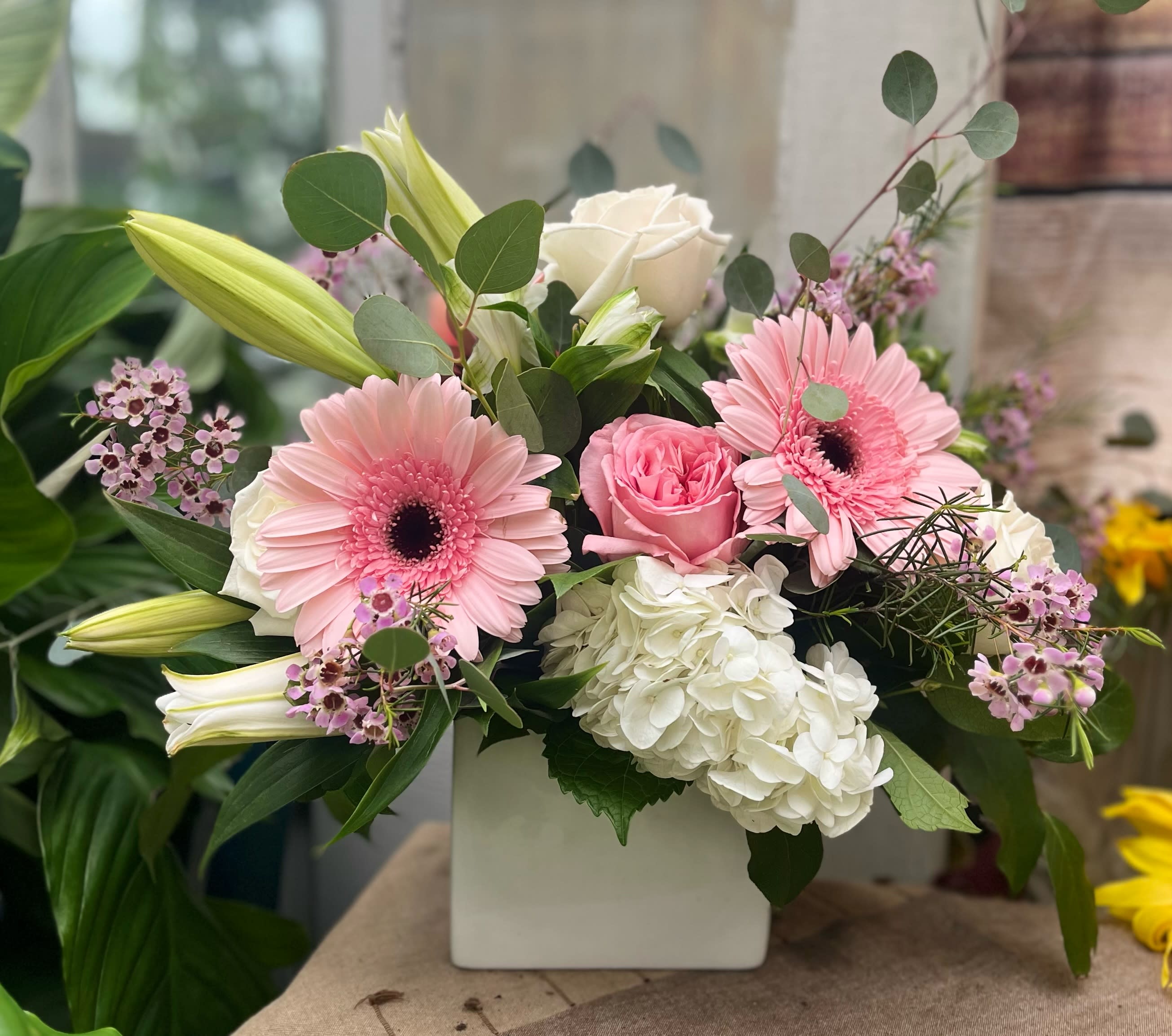 Pink gerbera daisies and roses in a white square vase