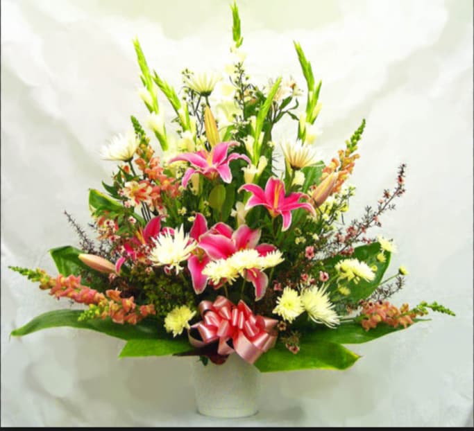 Pink lilies and white daisies in a white vase with a pink ribbon