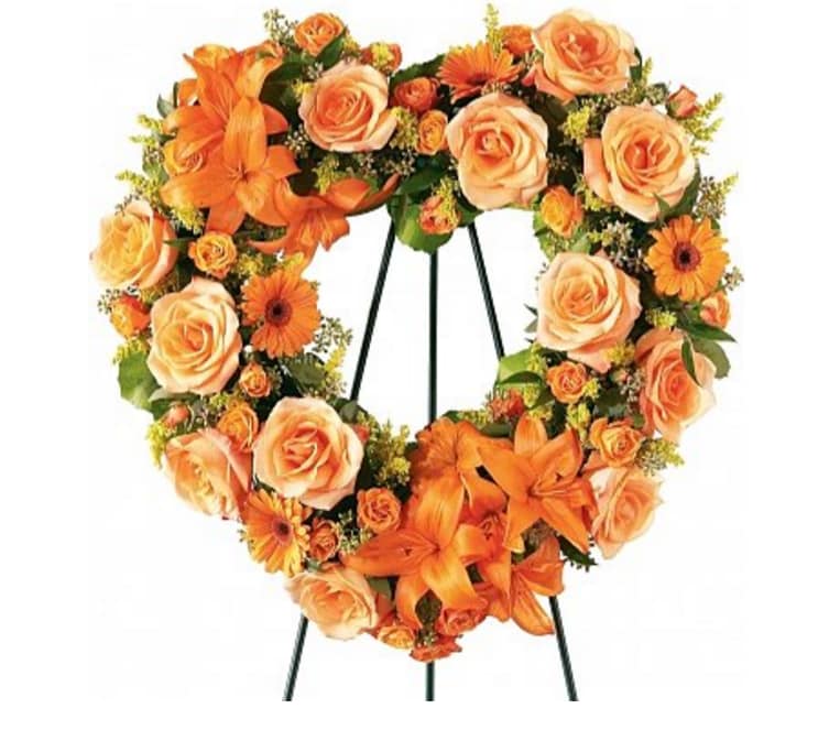 Heart-shaped floral wreath with orange roses and lilies on a stand